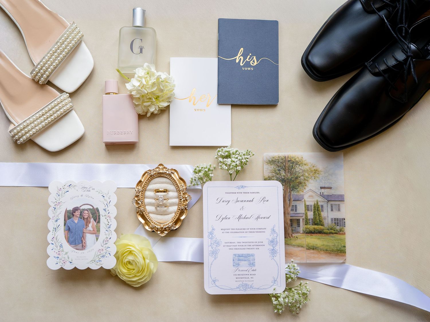 Elegant wedding flat lay featuring invitation suite, bridal heels, groom shoes, perfume, floral accents, and gold frame on neutral backdrop.