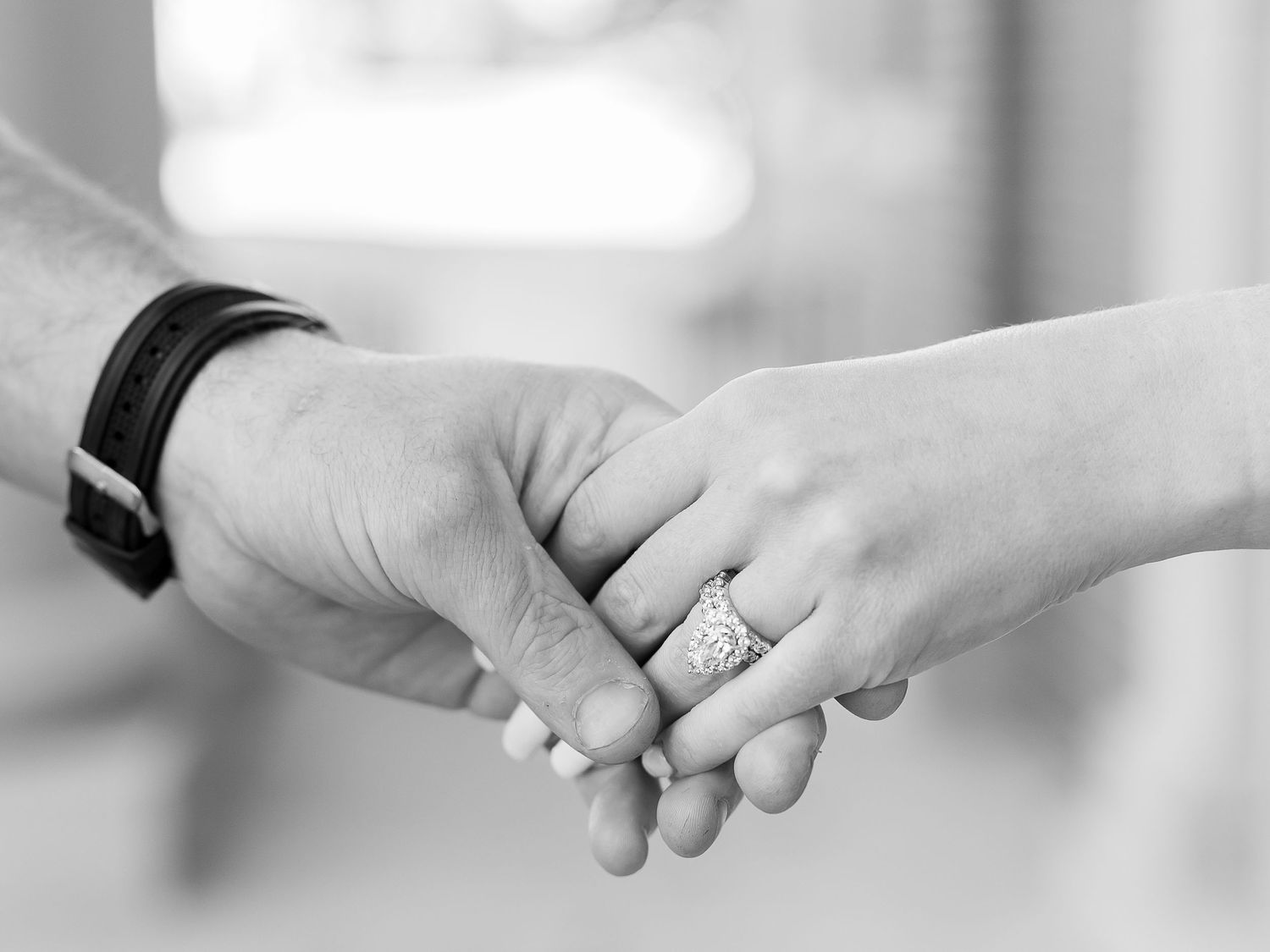 Two hands clasped together, one wearing a diamond ring, in a black and white image.