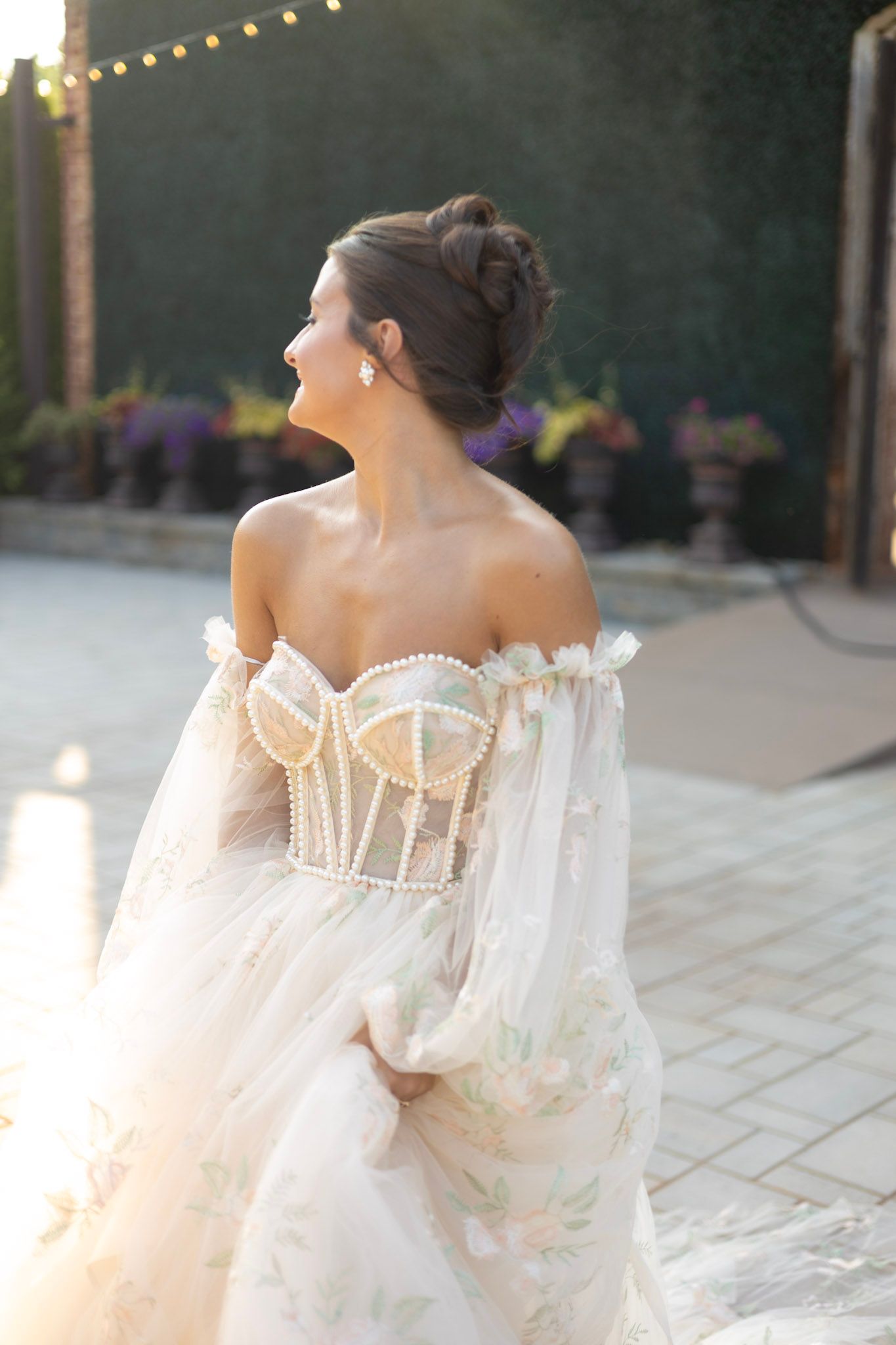 Ethereal off-shoulder wedding gown with delicate details captured in romantic outdoor setting.