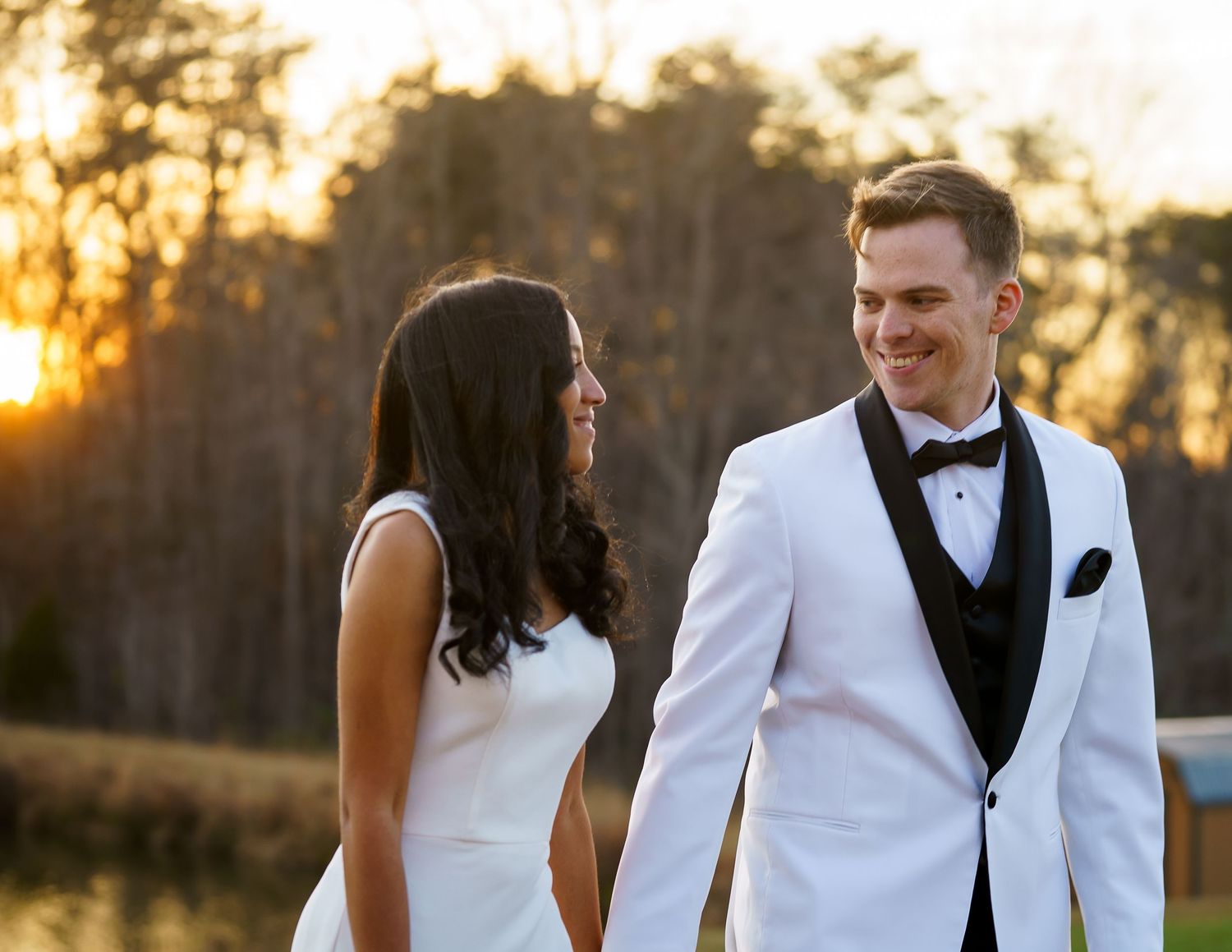 Bride and groom share a romantic moment outdoors at golden hour, with a glowing sunset and trees in the background.