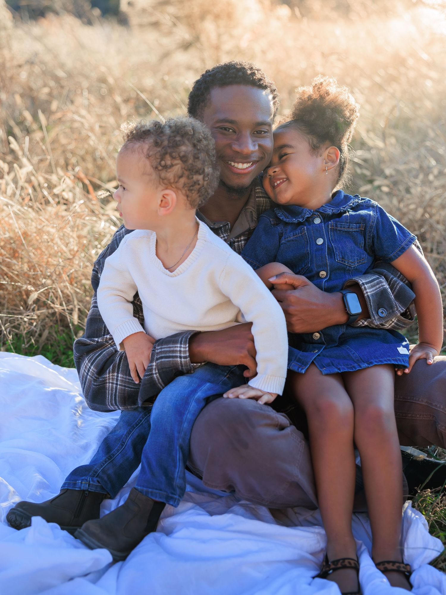 A group of people sitting together outdoors on a blanket sharing a tender moment in warm sunlight.