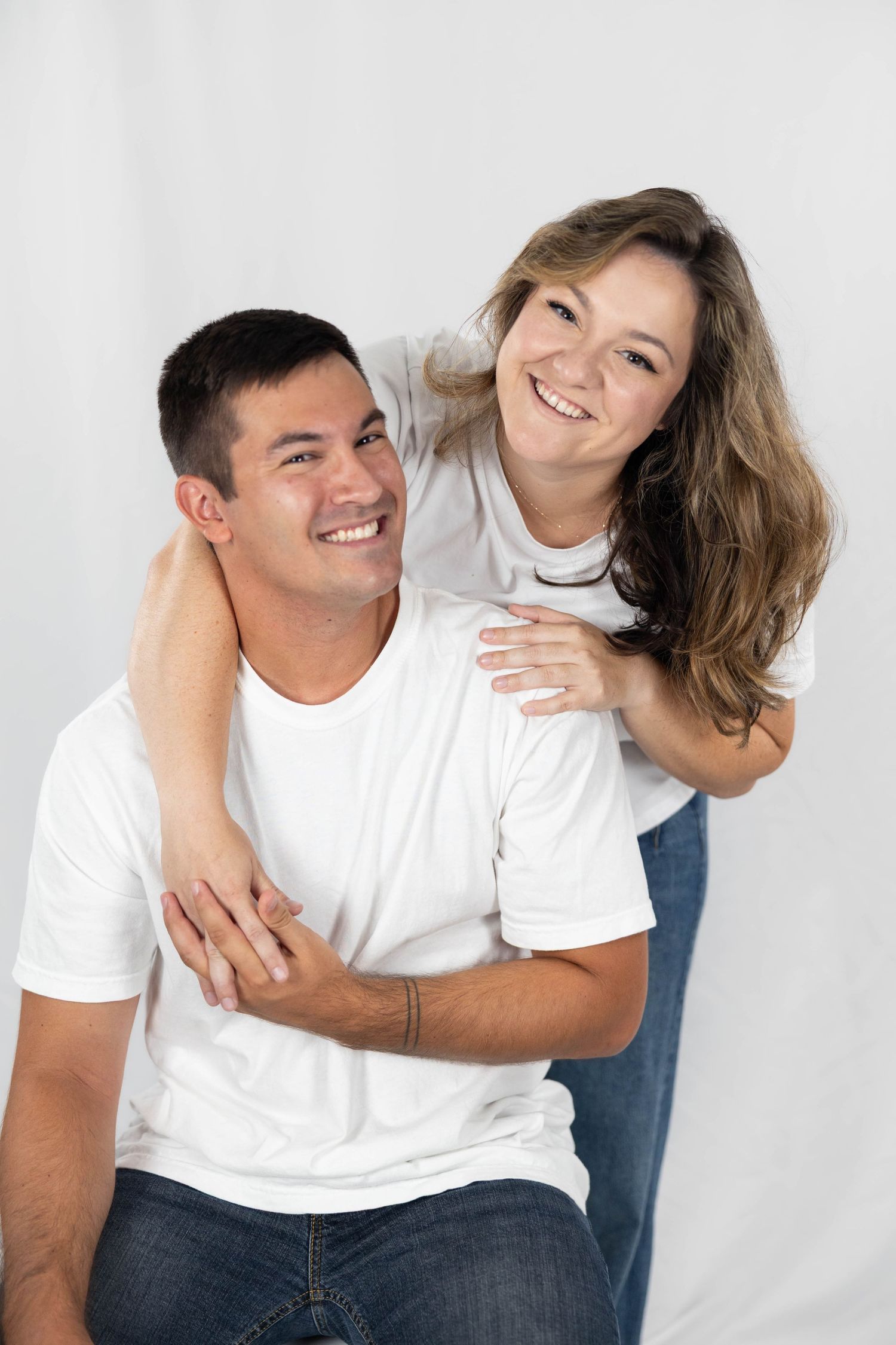 A couple in white shirts and jeans playfully pose and laugh together in four candid studio photos against a white background.