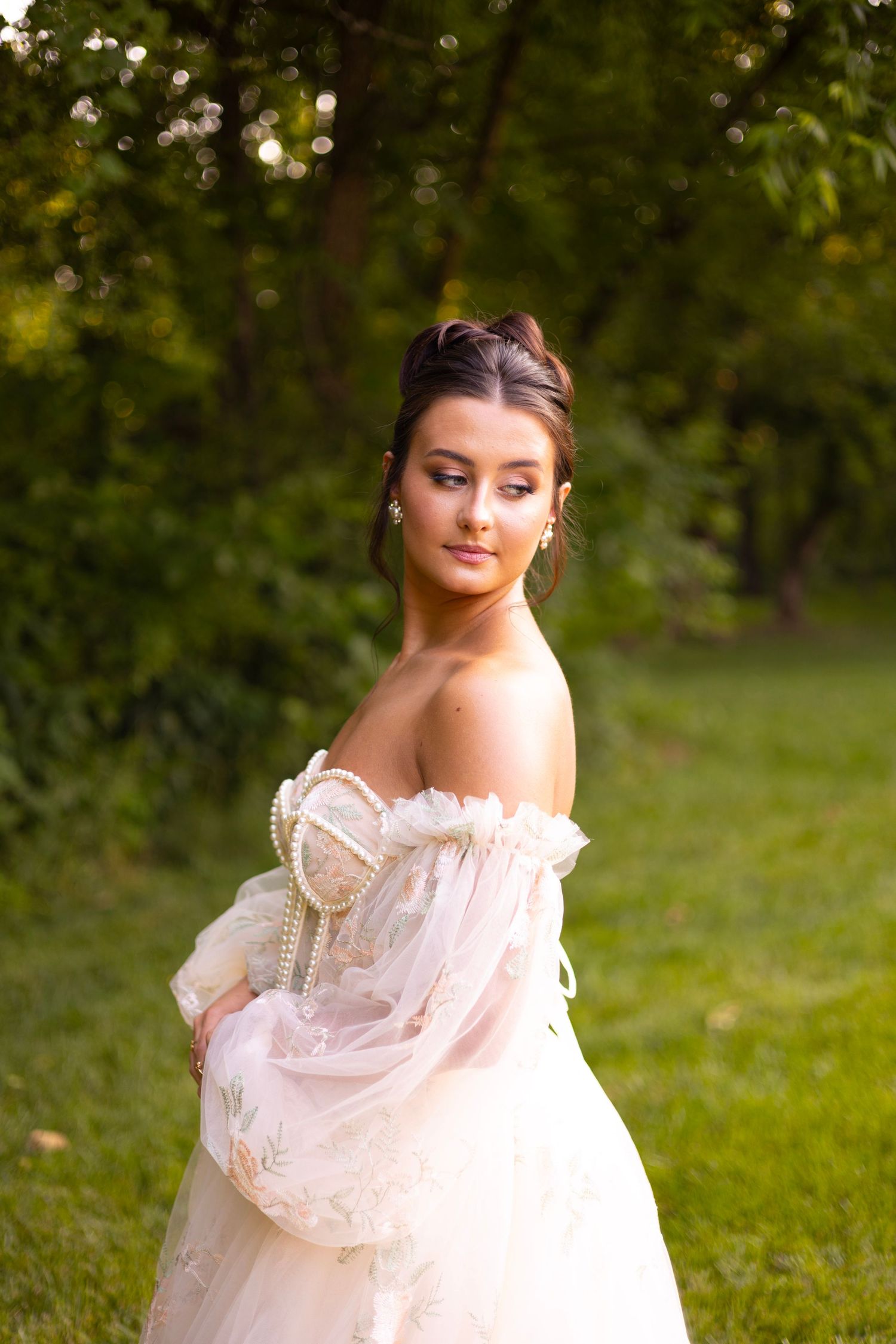 A bride in a delicate off-shoulder gown poses against a lush garden backdrop.