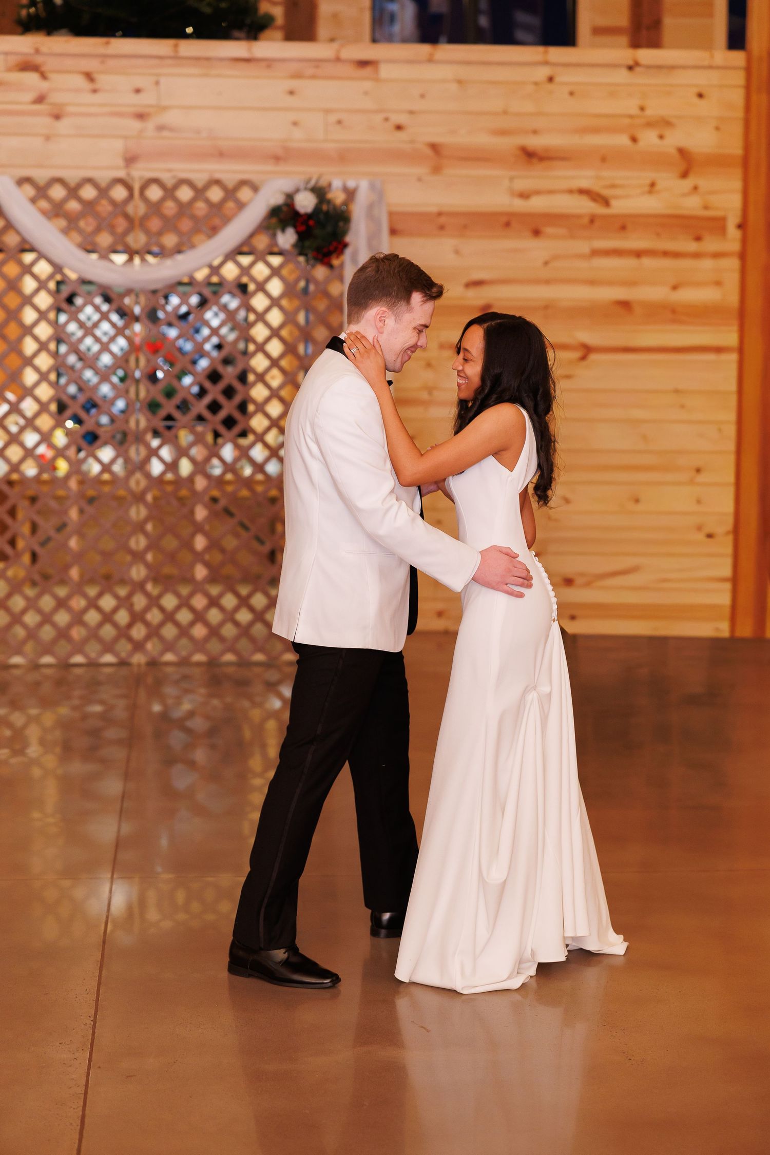 A bride and groom share their first dance in a warmly lit wooden reception hall.
