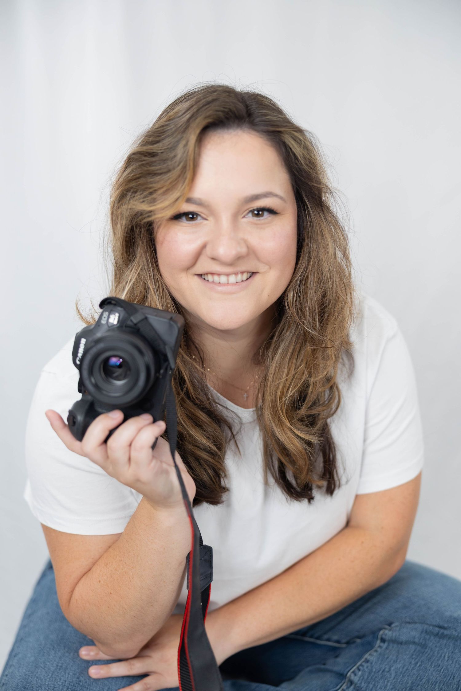 Photographer in white t-shirt and jeans holds camera while posing in studio against light background in four different poses.