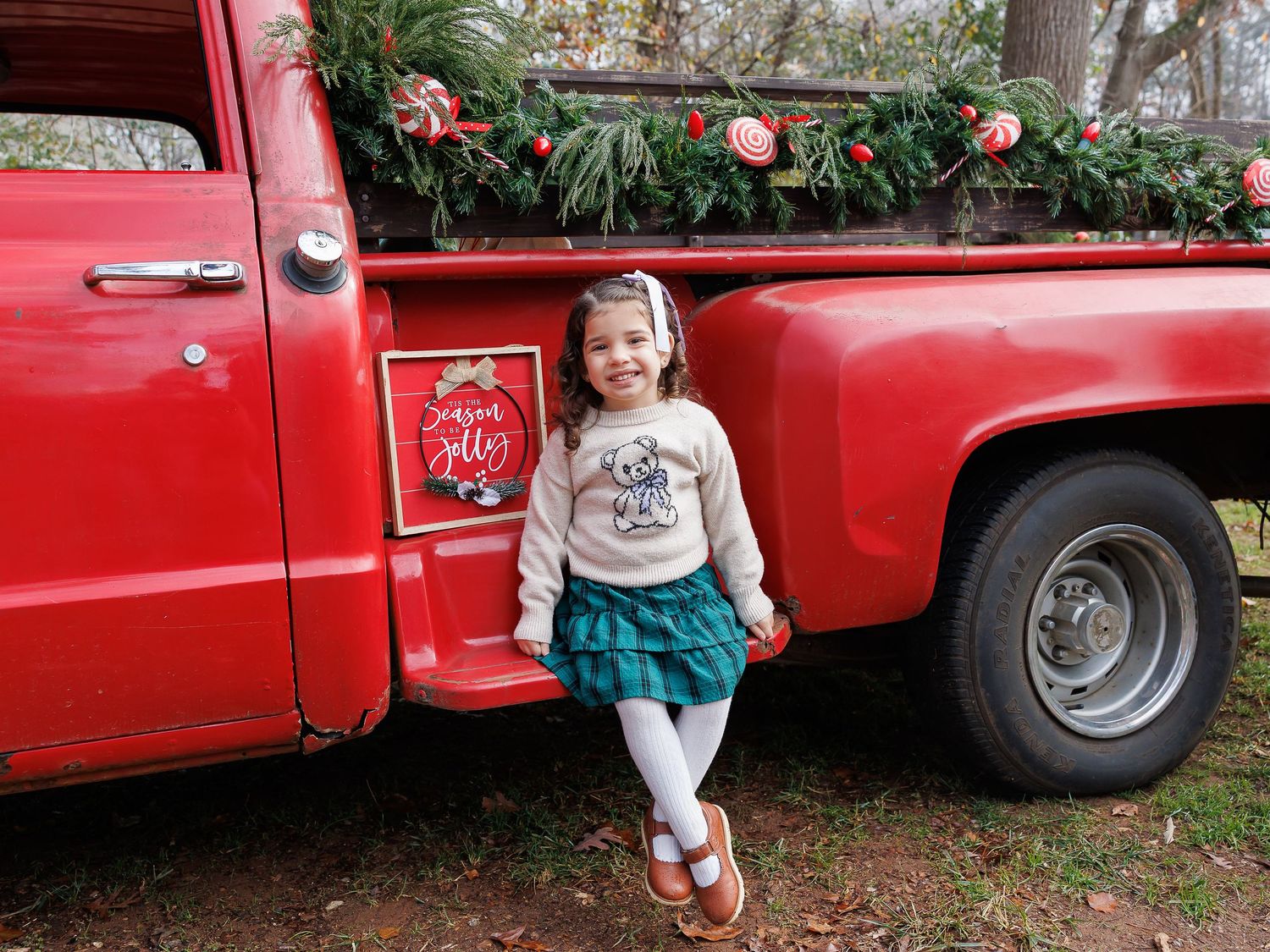 Vintage red pickup truck decorated with holiday greenery and ornaments parked in a rustic outdoor setting.