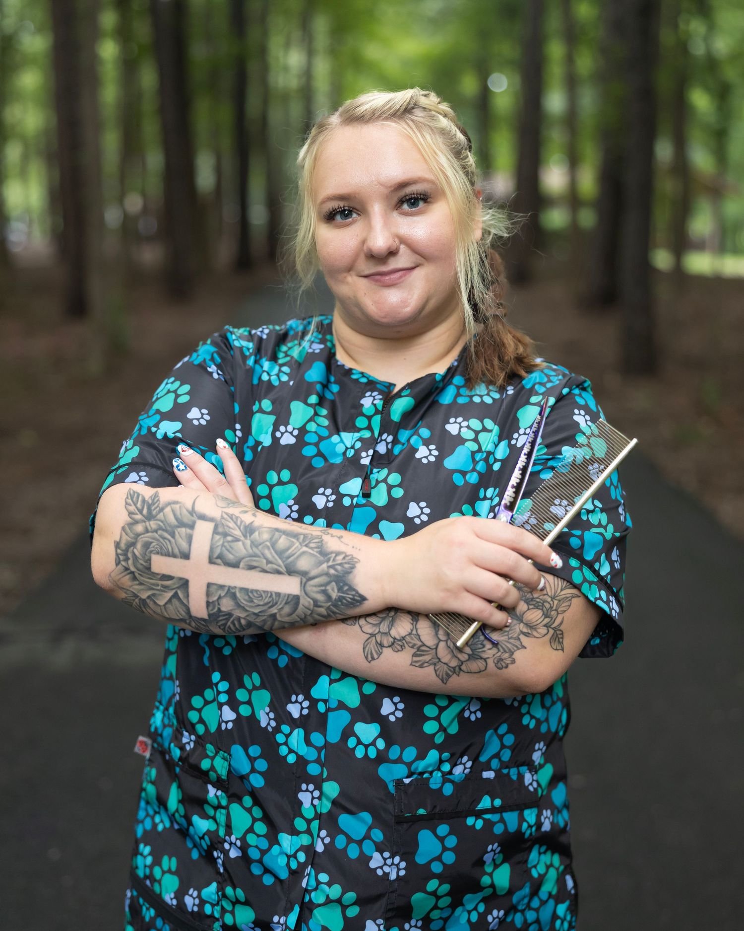 Medical professional in blue paw print scrubs with arm tattoos holding tools in a wooded setting.