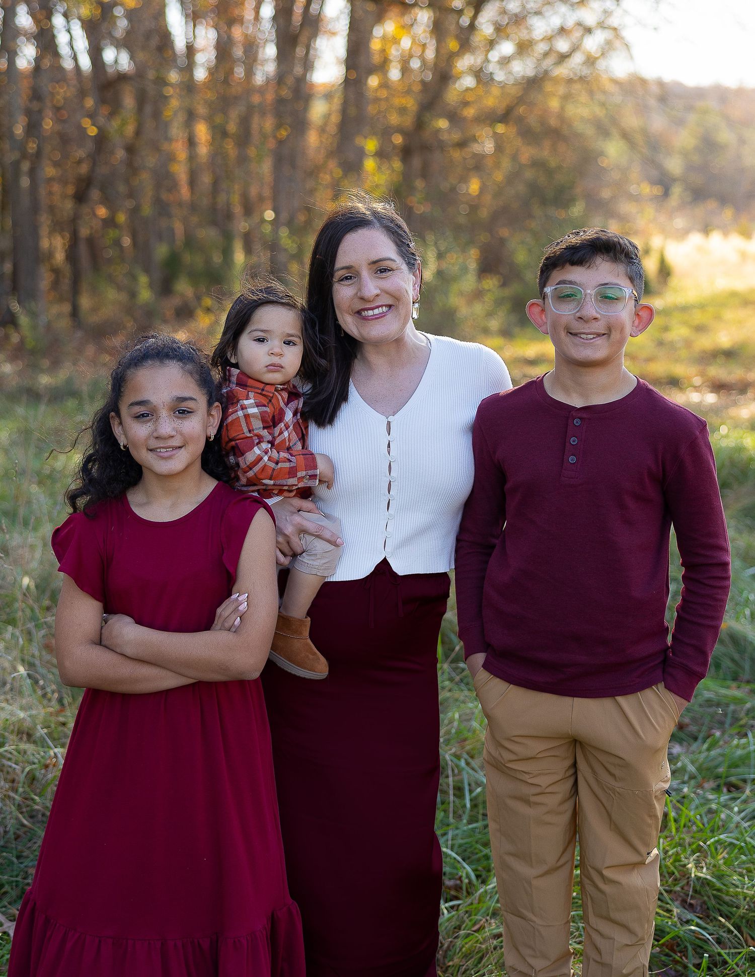 Family group wearing coordinated burgundy and neutral outfits smiles together during a fall photo session.