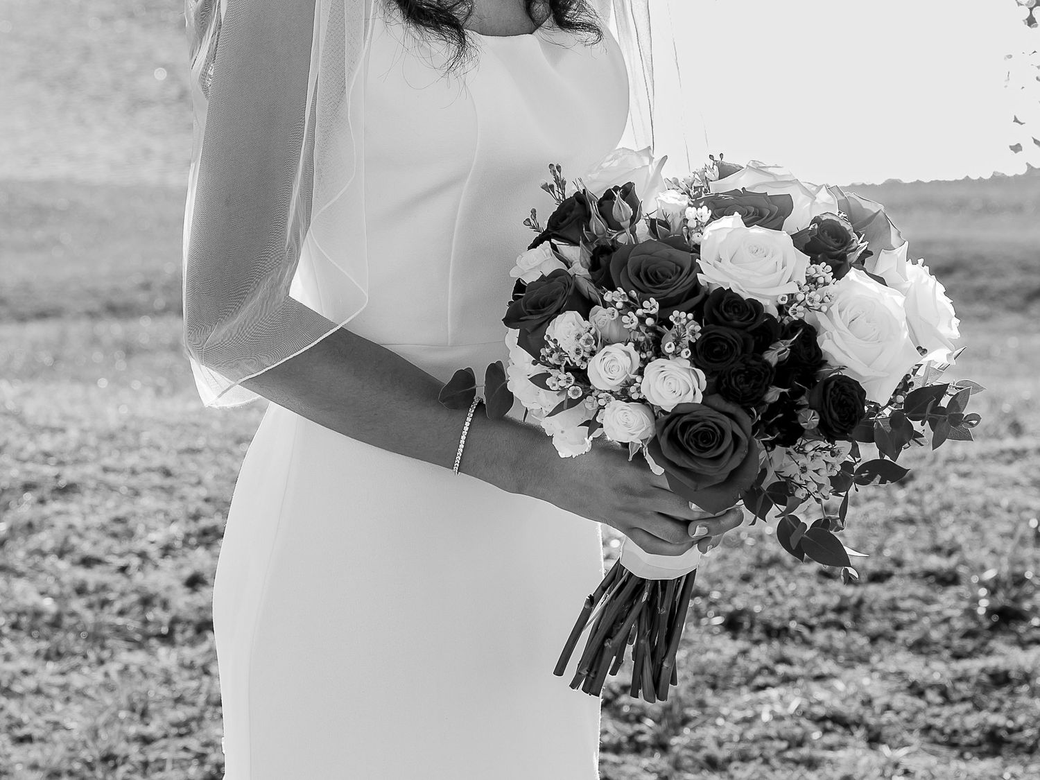 Bride in white gown holding elegant bouquet of roses in black and white wedding photo outdoors.
