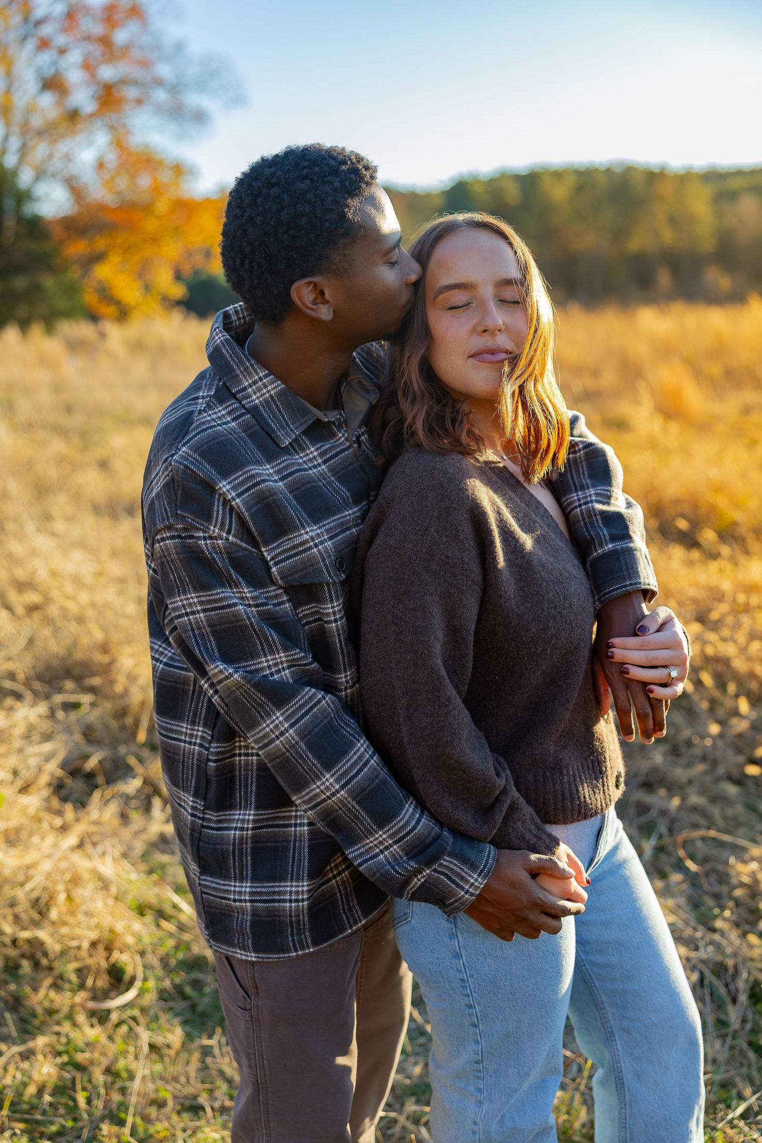 Couple embracing in a golden autumn field during sunset while sharing drinks outdoors.