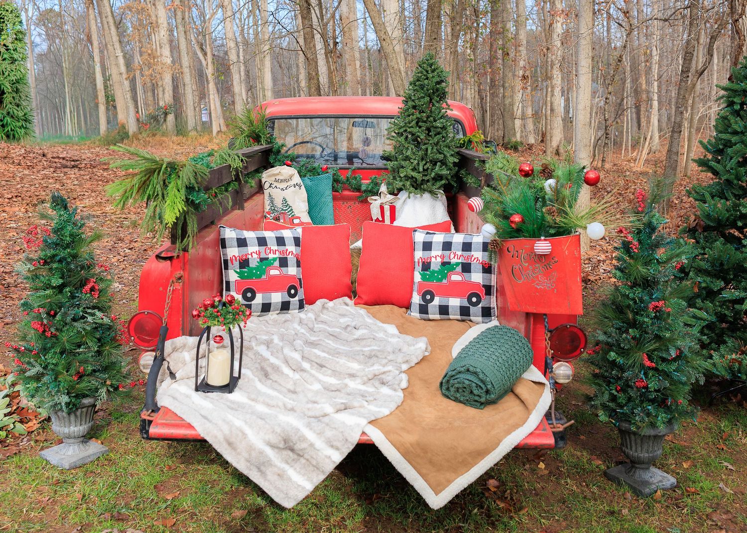 A cozy outdoor seating area with plaid pillows and red cushions nestled among evergreen trees in a winter forest setting.