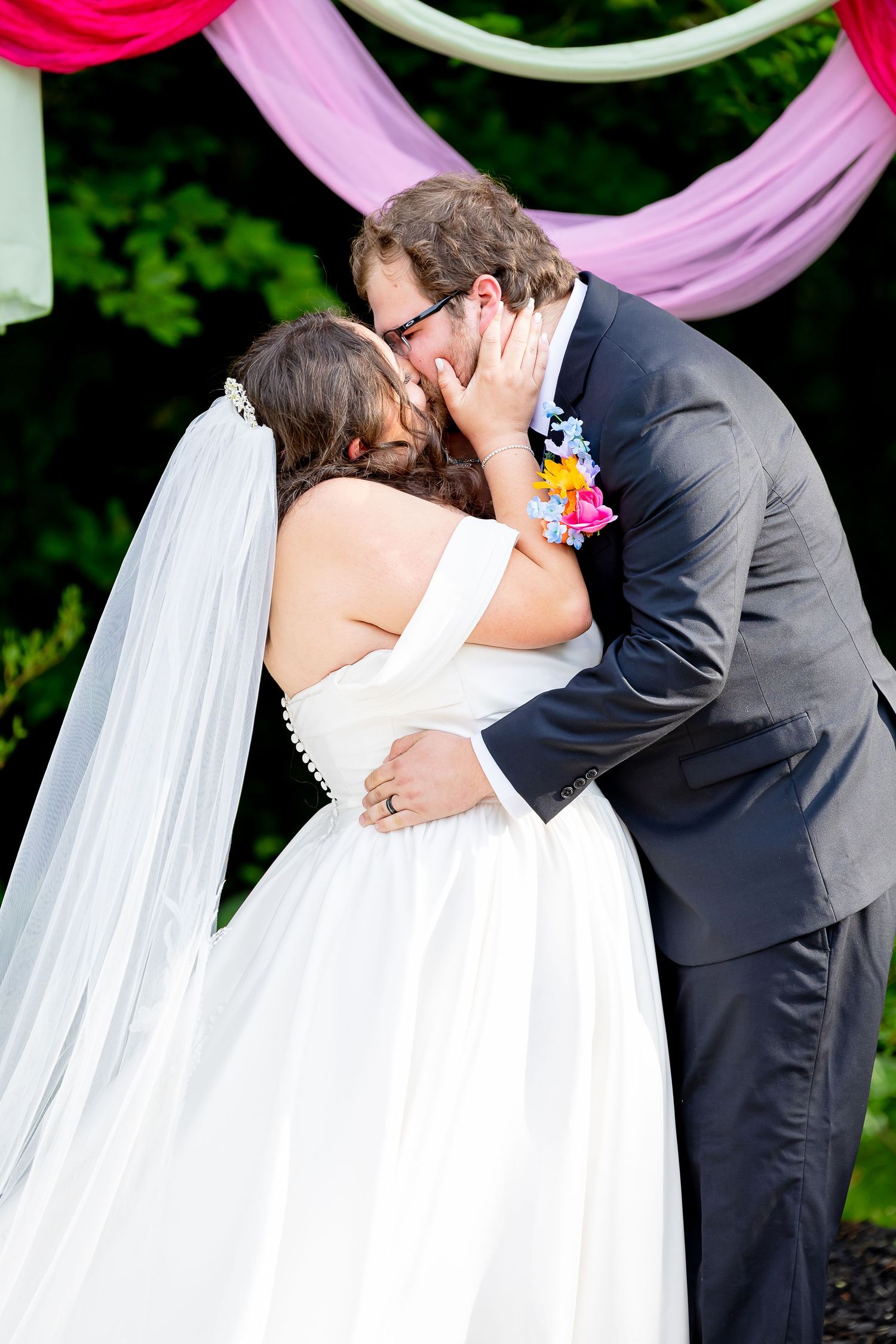 Bride and groom sharing their first kiss at the altar decorated with pink and white draped fabric.