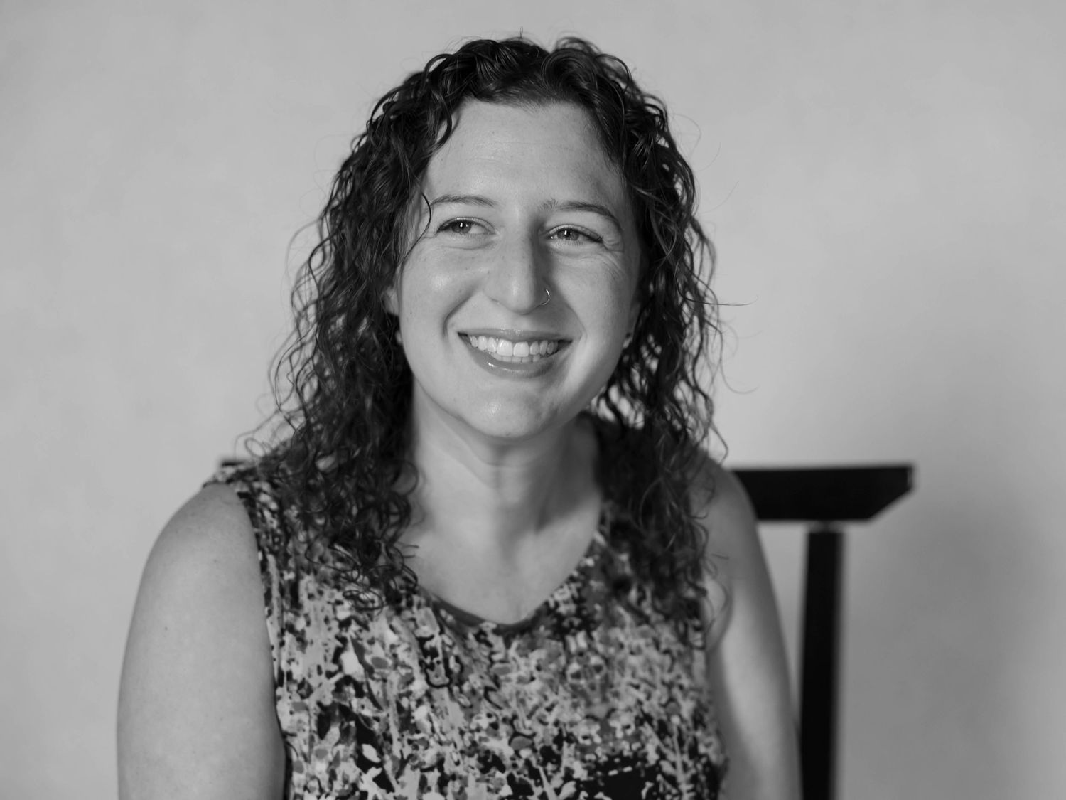 Black and white portrait of a person with curly dark hair wearing a floral sleeveless top and smiling at the camera.