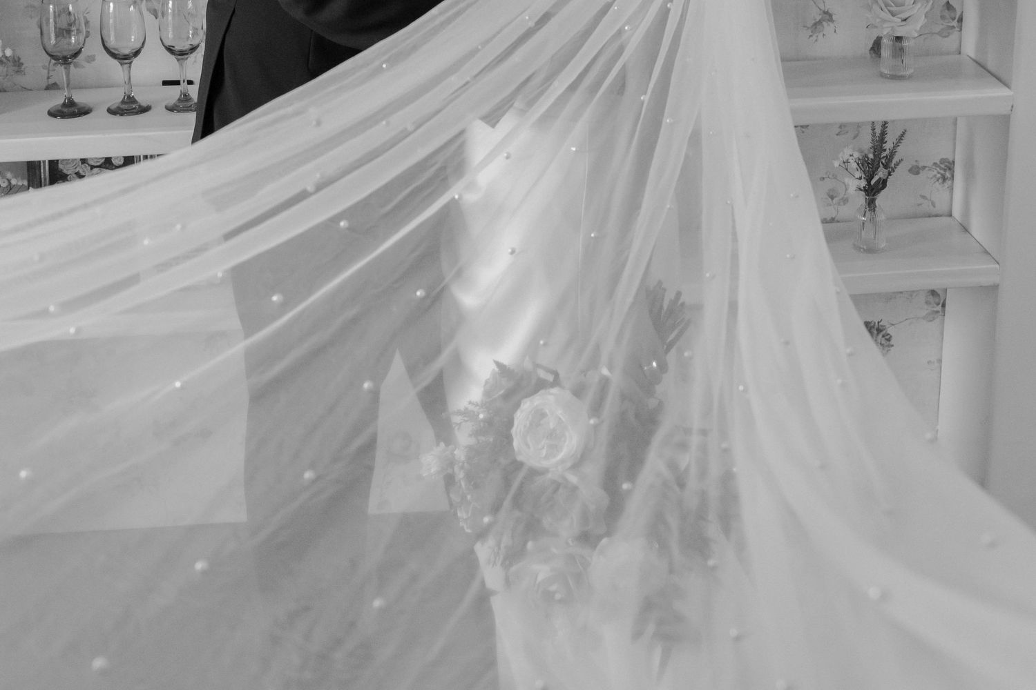 A flowing white wedding dress train with delicate lace details spreads elegantly across a light-colored floor.