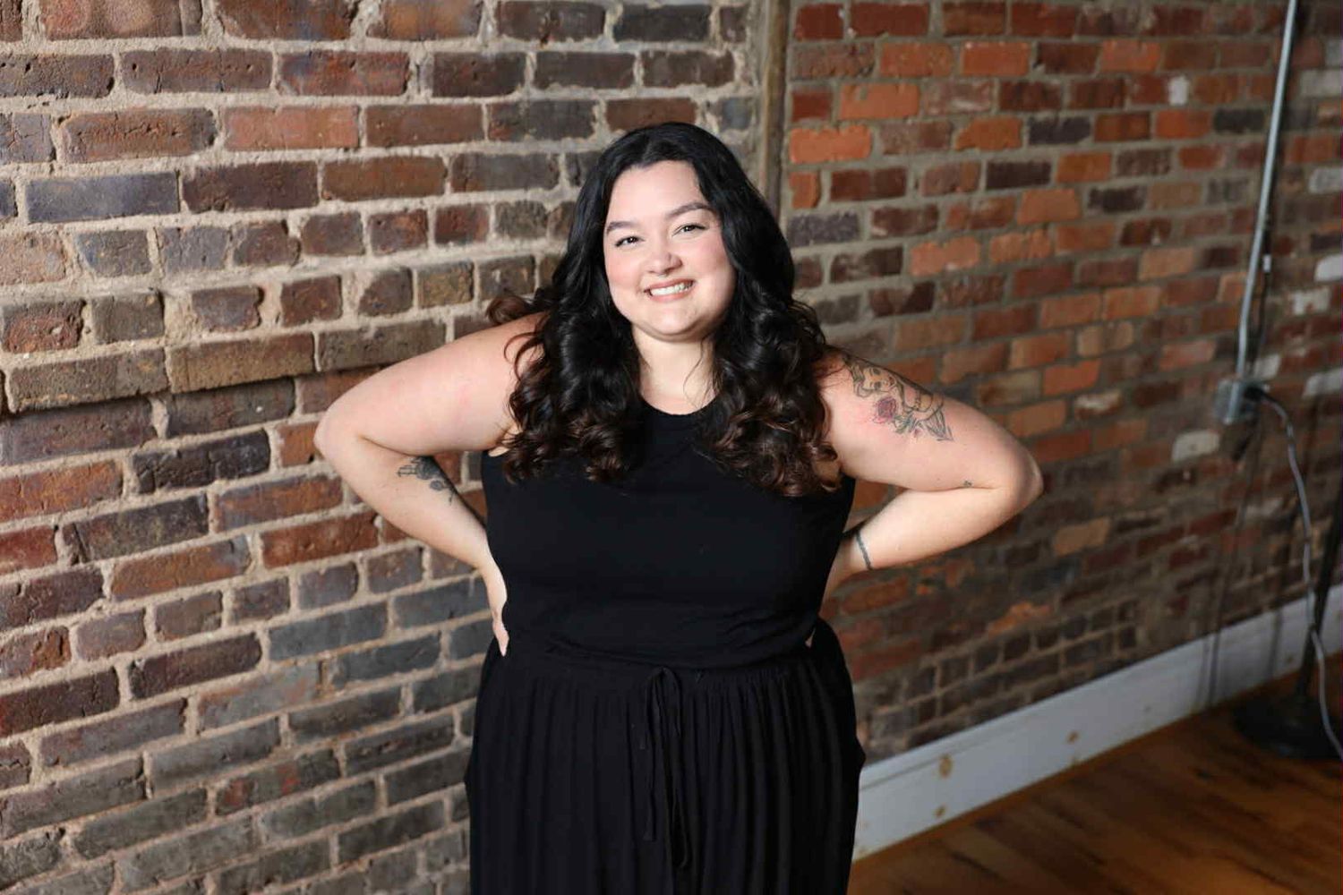 Portrait session against exposed brick wall showing elegant posing in black attire.