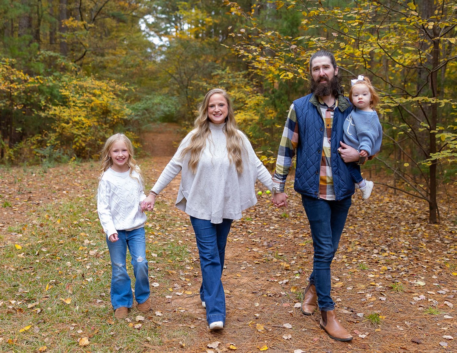 A group walks together on a leaf-covered forest path during autumn while wearing matching denim outfits.
