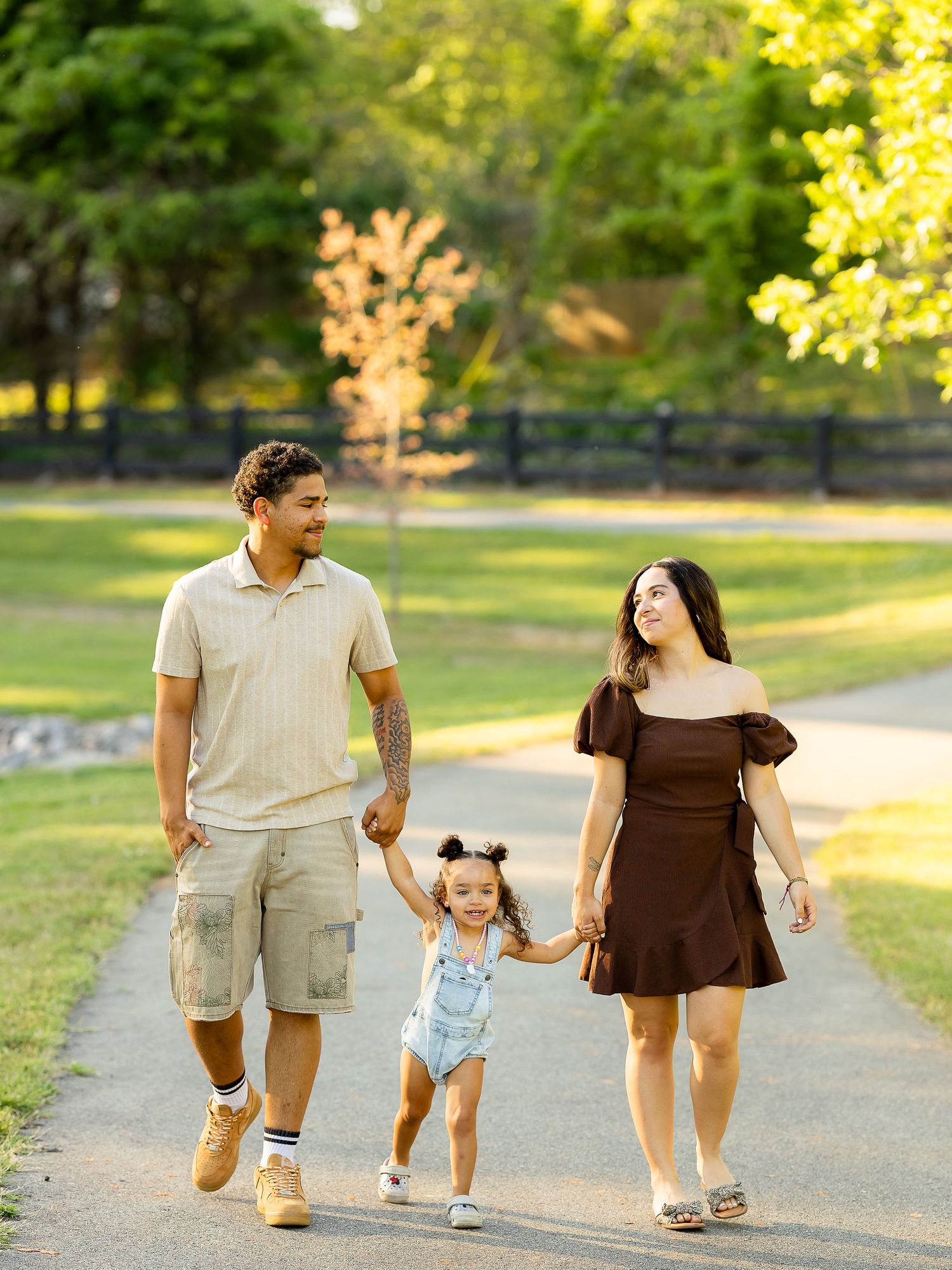 Young family walking hand-in-hand along a park path in warm golden sunlight.