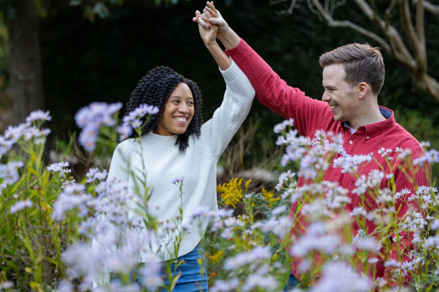 Happy couple enjoying a romantic walk through a blooming garden with purple and pink flowers.