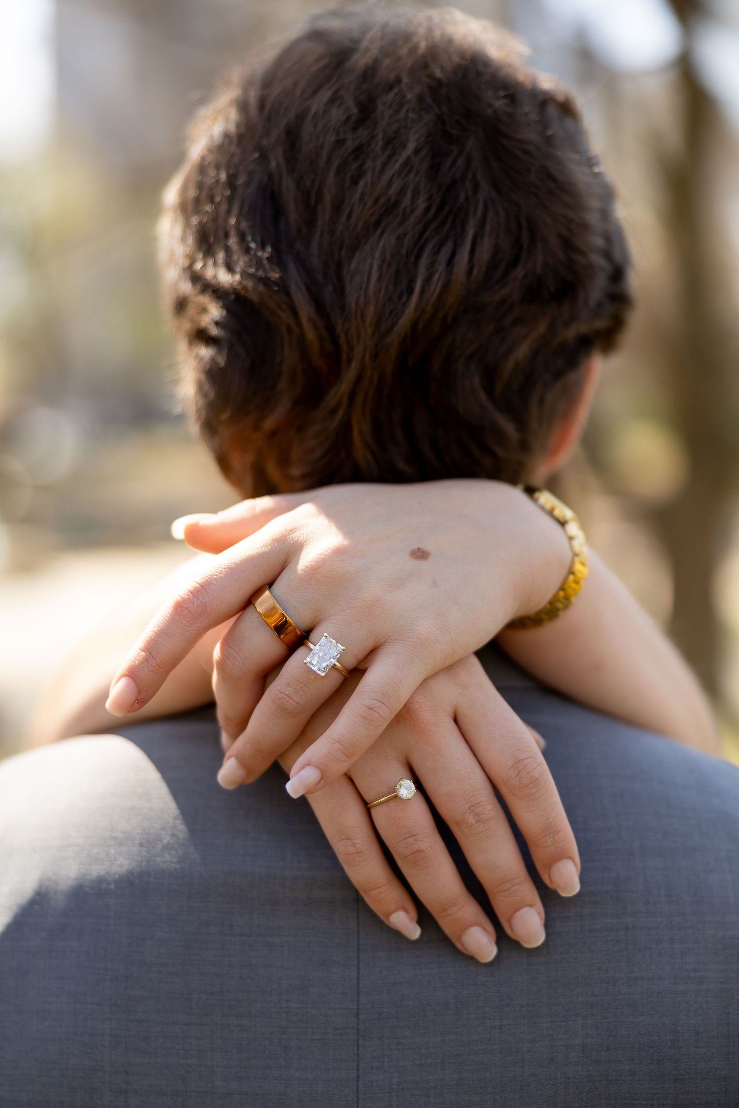 Close-up shots of hands with an engagement ring resting on a shoulder in a grey suit.