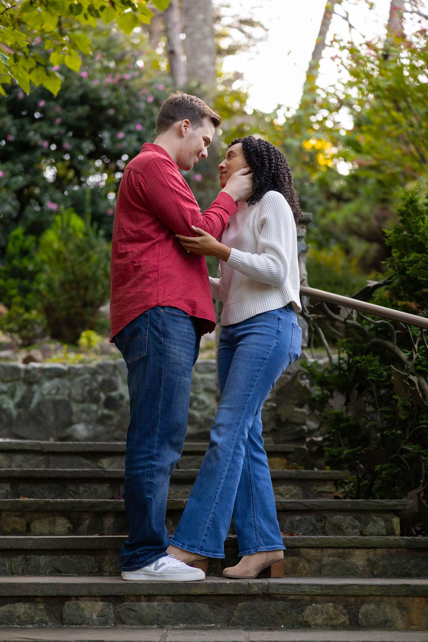 A romantic couple shares tender moments on stone steps surrounded by lush greenery in a garden setting.