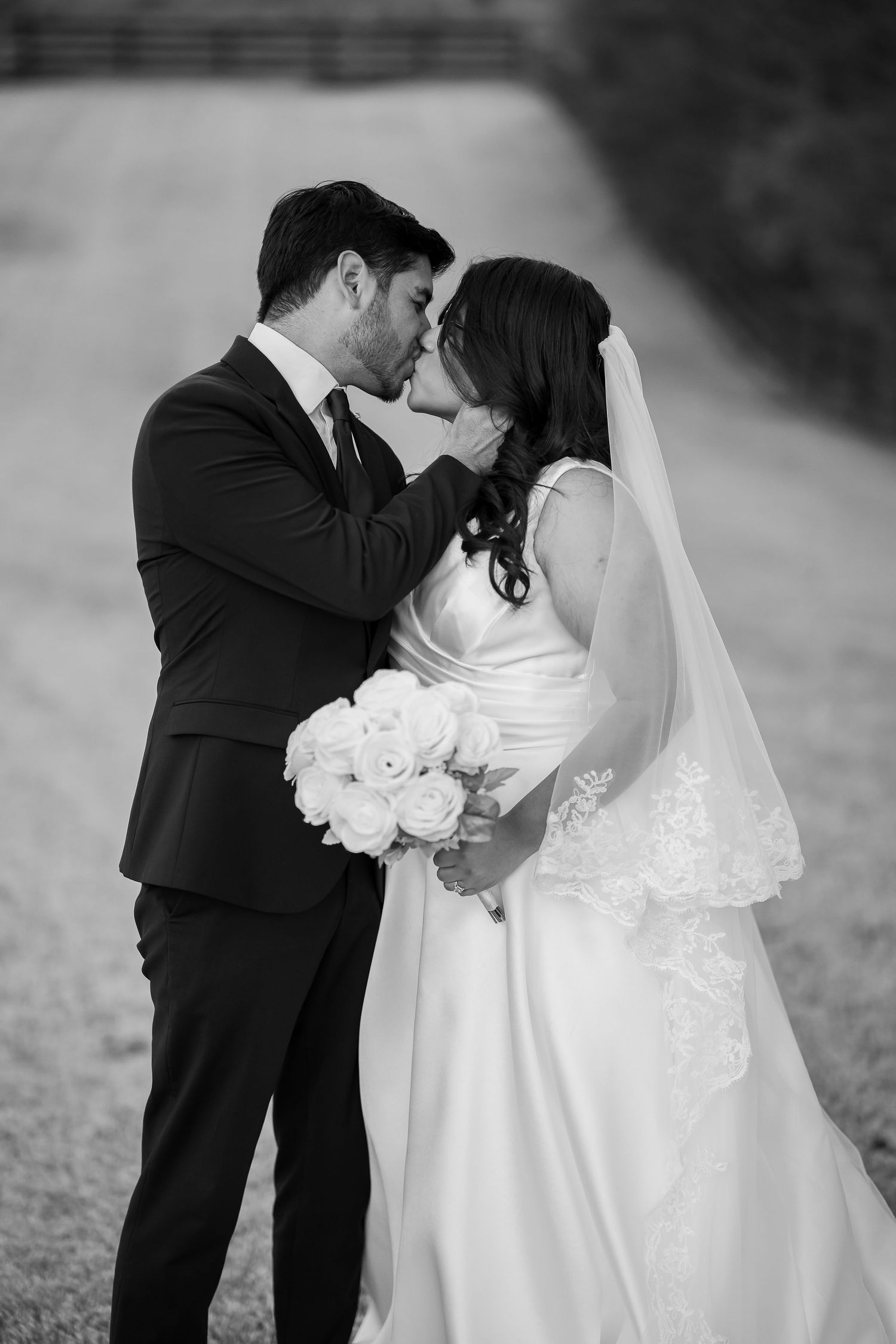 Black and white photo of bride and groom sharing a tender kiss, bride holding white rose bouquet.