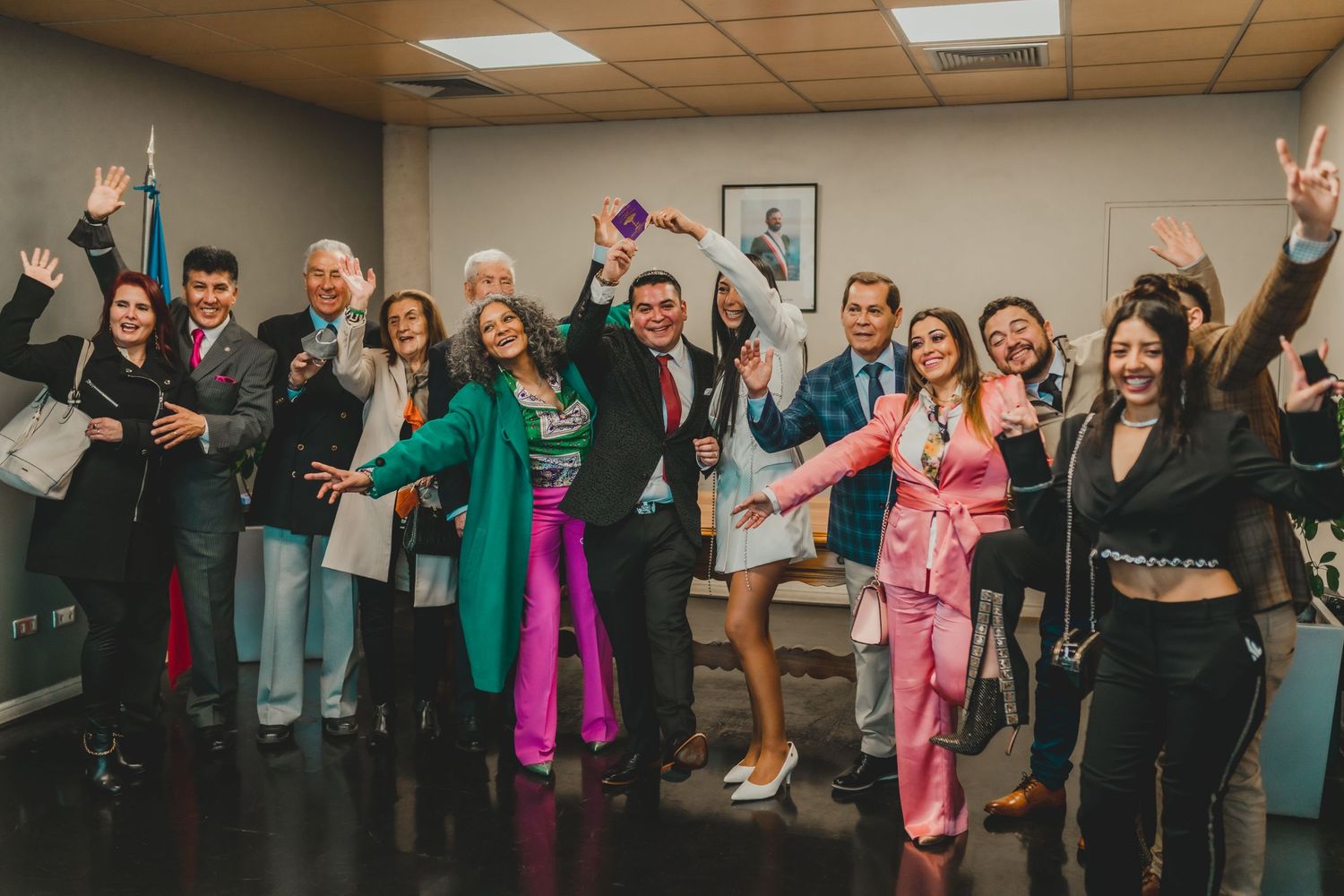 A group of energetic people posing together in a hallway, making celebratory gestures and wearing colorful outfits.
