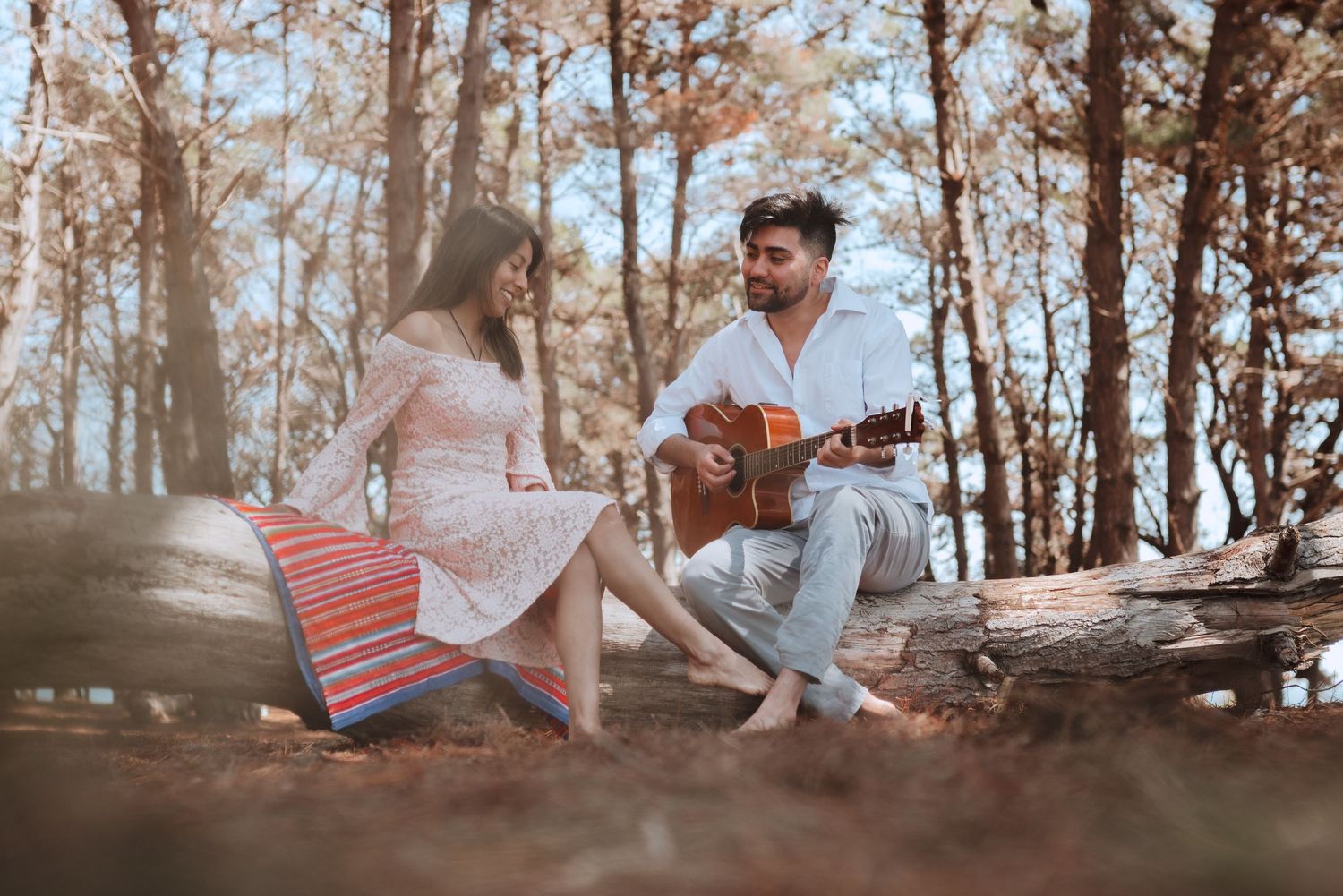 A romantic forest picnic scene with an acoustic guitar and striped blanket on autumn ground.