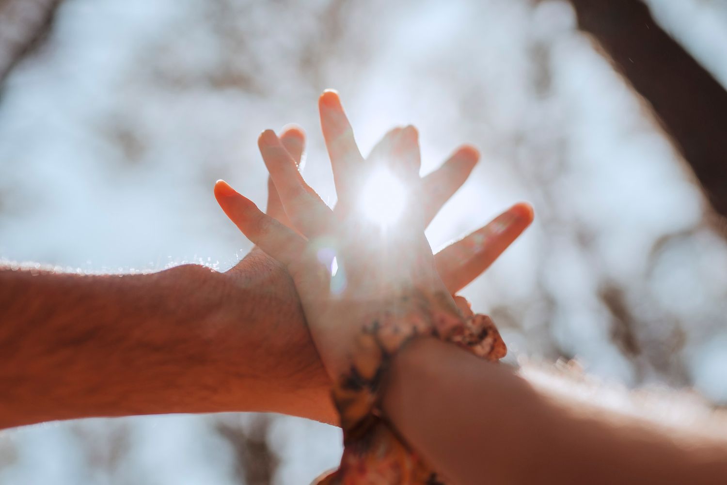 Hands reaching together toward sunlight creating a starburst effect through spread fingers.