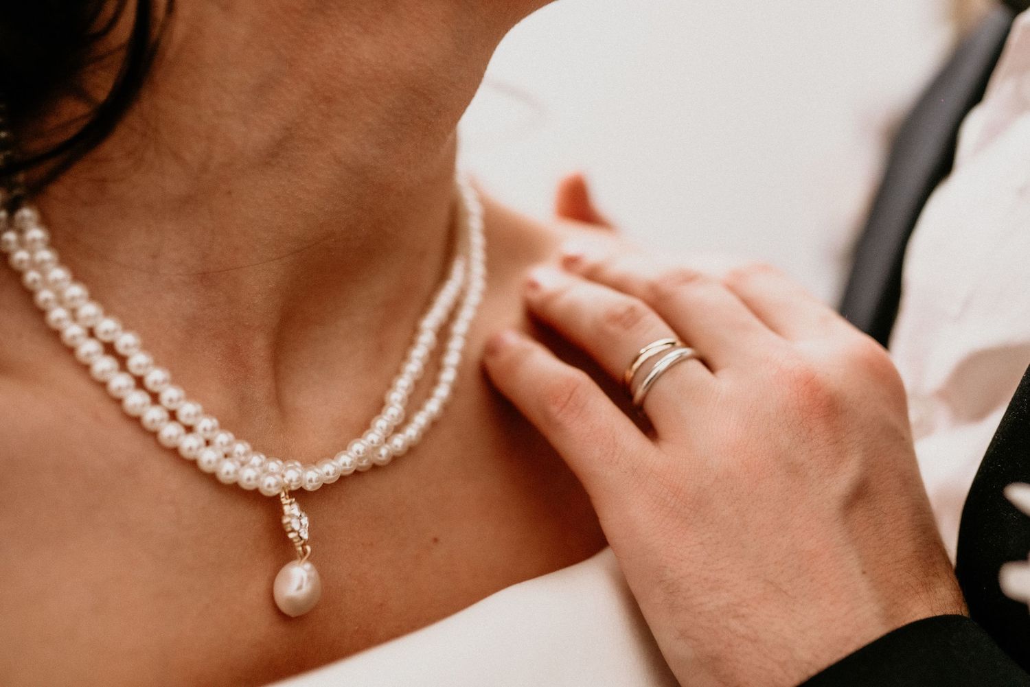 Person wearing a pearl necklace and elegant bridal jewelry holds their hand near their neck in delicate bridal pose.