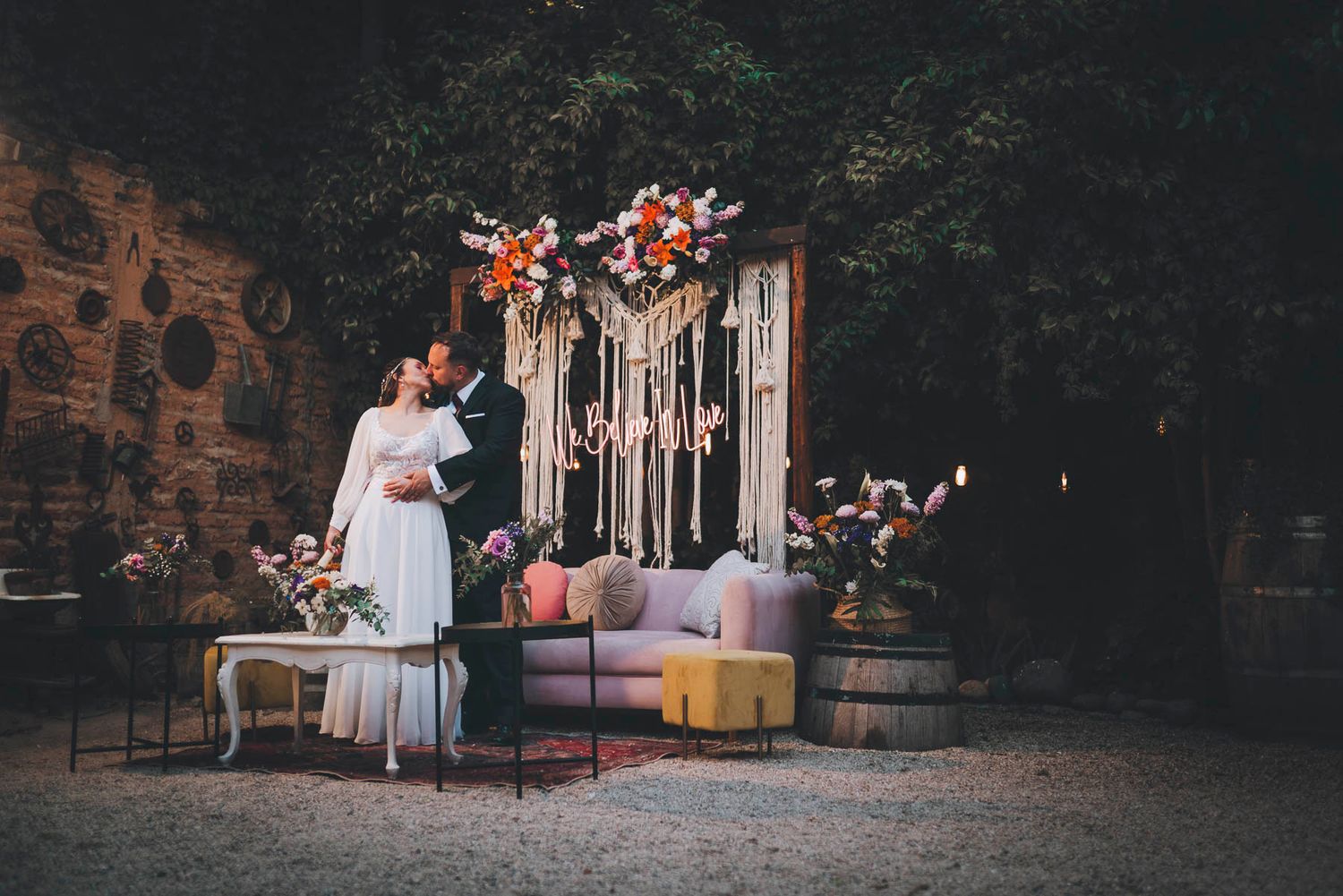 A romantic outdoor wedding scene with a vintage couch and macrame backdrop decorated with coral and cream flowers.