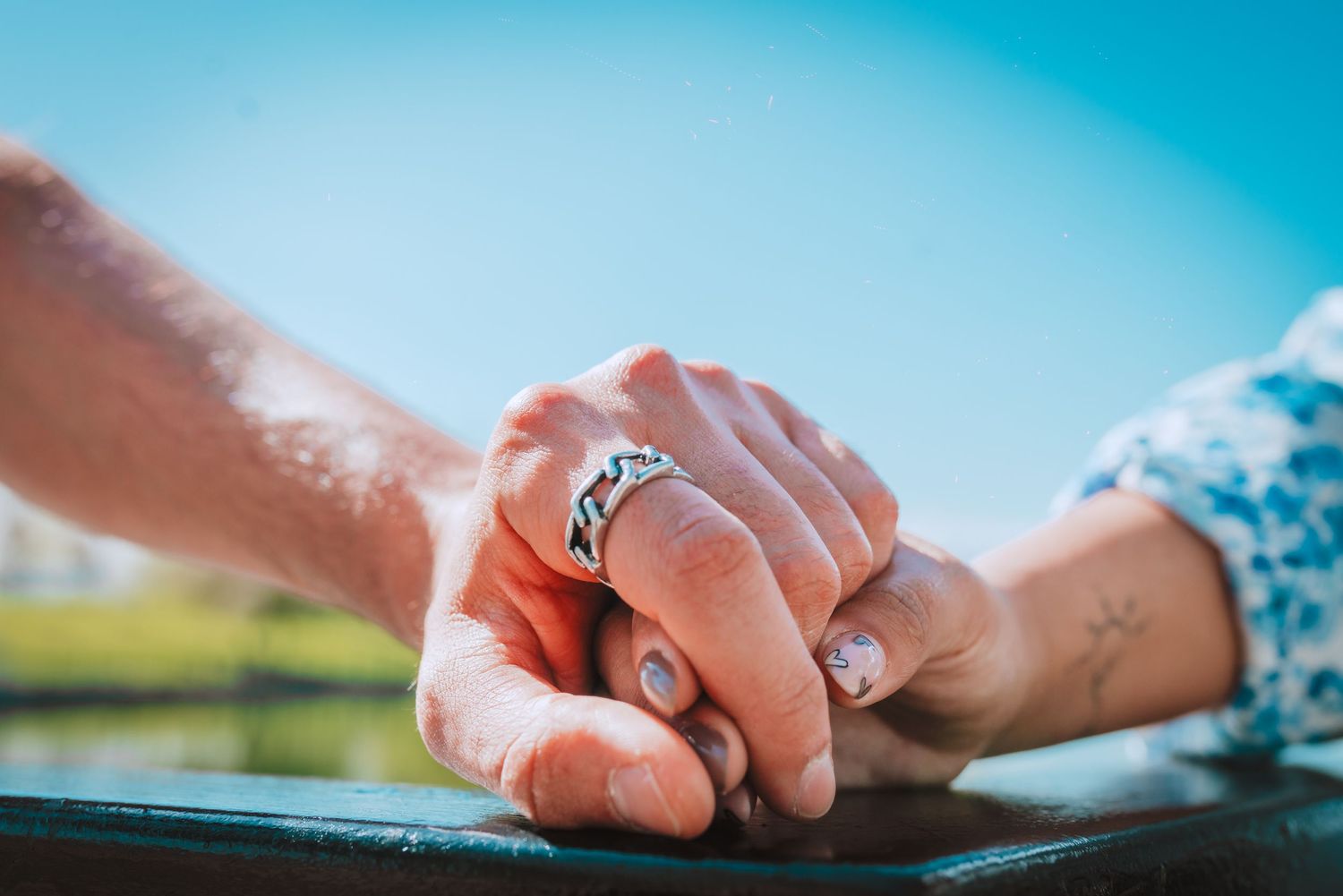 Close-up of intertwined hands with an engagement ring in natural sunlight.
