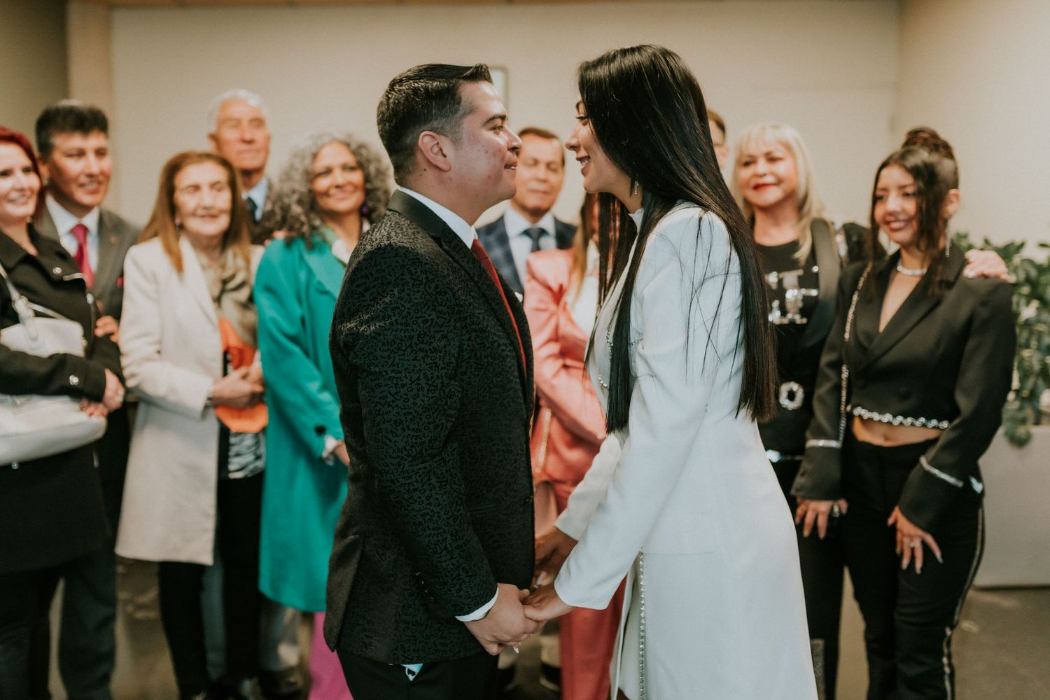 A couple shares their first kiss at a wedding ceremony while guests look on with joy in an indoor venue.