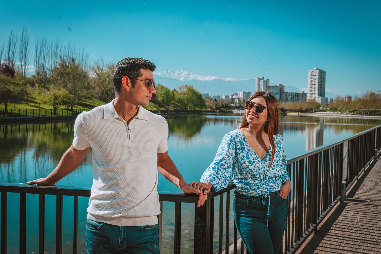A couple sharing a lighthearted moment while walking along a lakeside path with city views.
