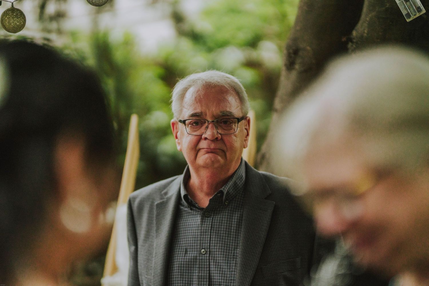 A person in glasses wearing a grey button-down shirt at a social gathering.