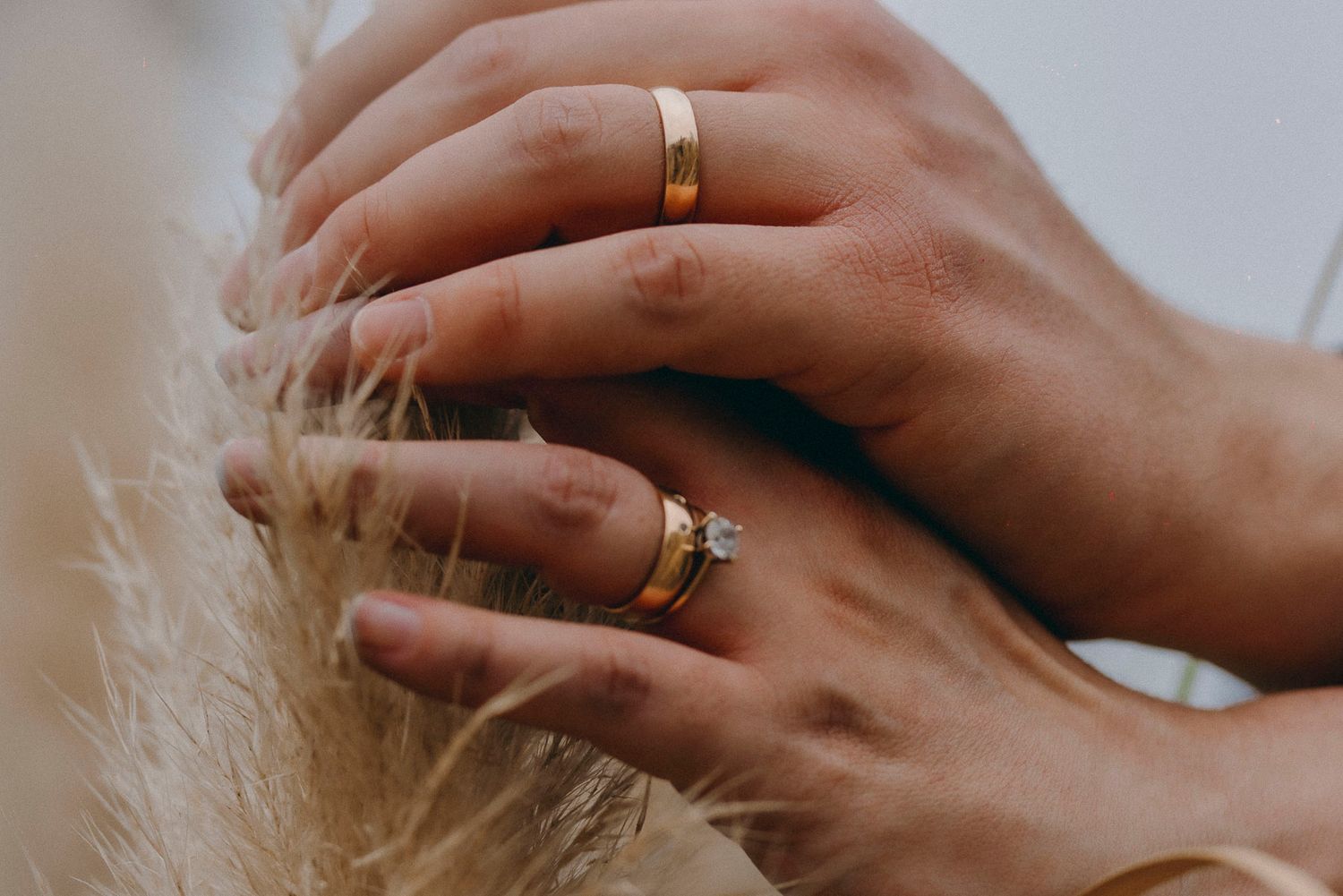 Close-up of hands wearing wedding rings against a neutral background.