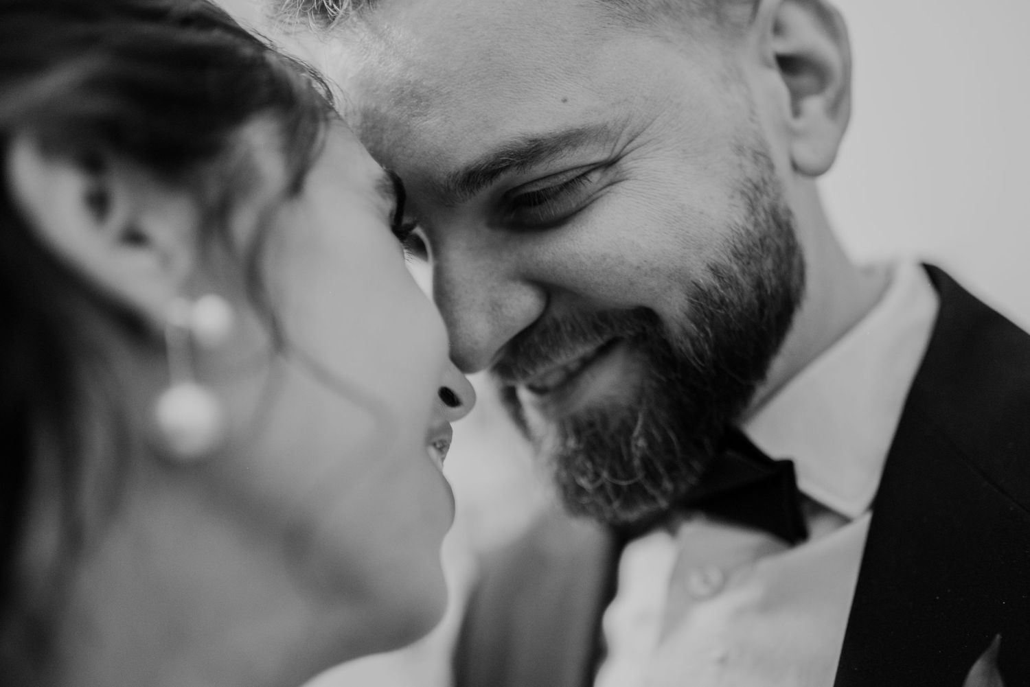 Black and white close up of tender moment between bride and groom sharing an intimate smile in formal wedding attire.