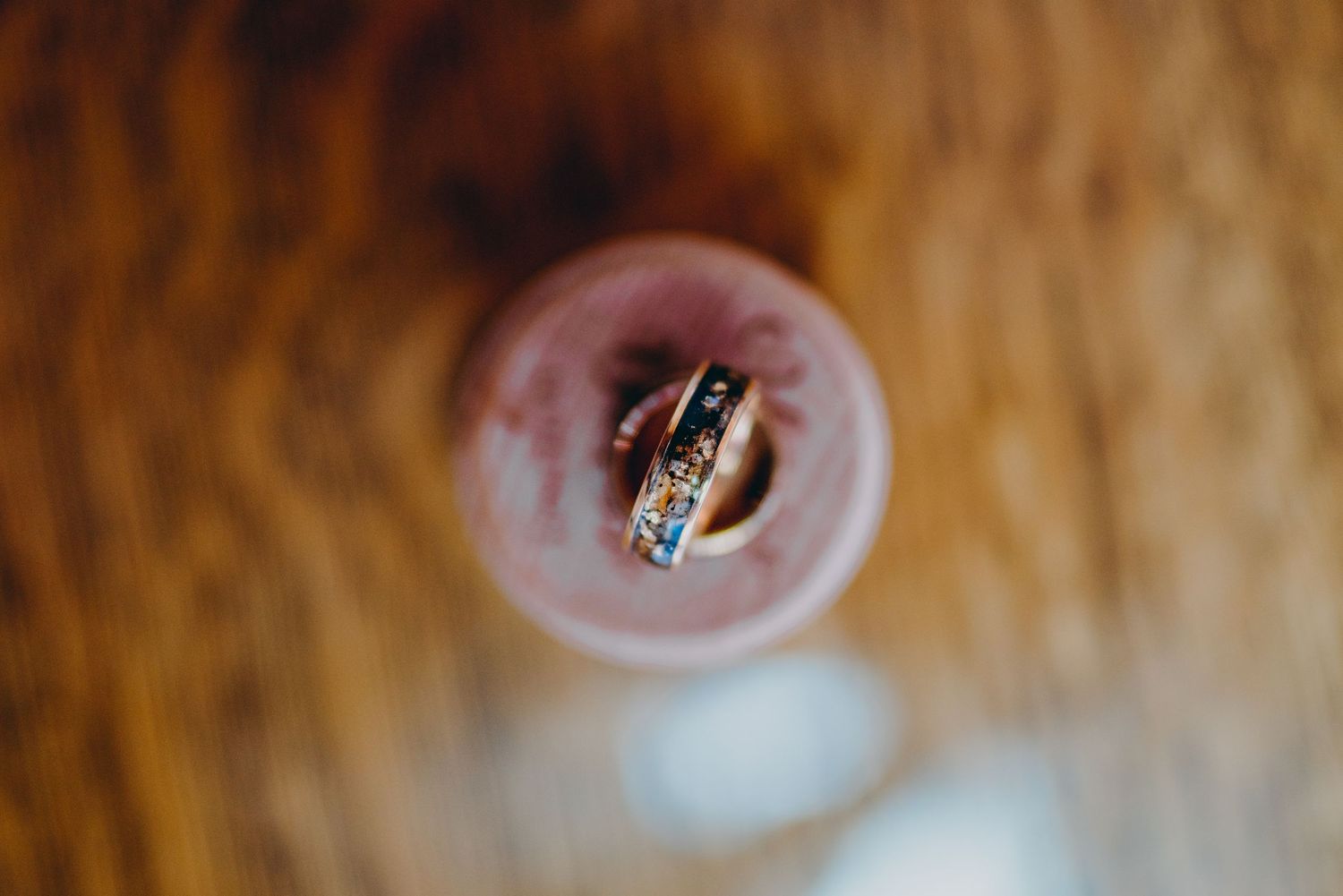 Close-up shot of a wedding ring balanced on top of a champagne glass with warm wooden backdrop.