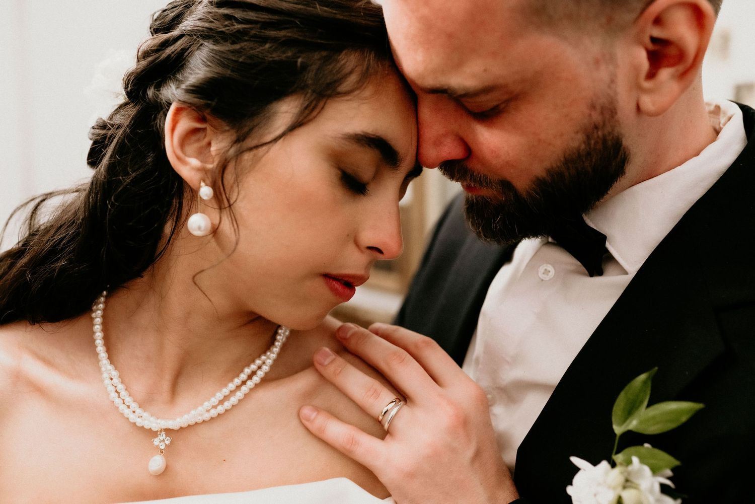 Intimate wedding photo showing romantic close-up moment with pearl necklace and boutonniere details.