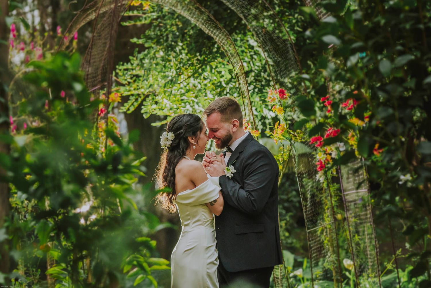 A romantic moment under a floral garden arch surrounded by lush greenery.