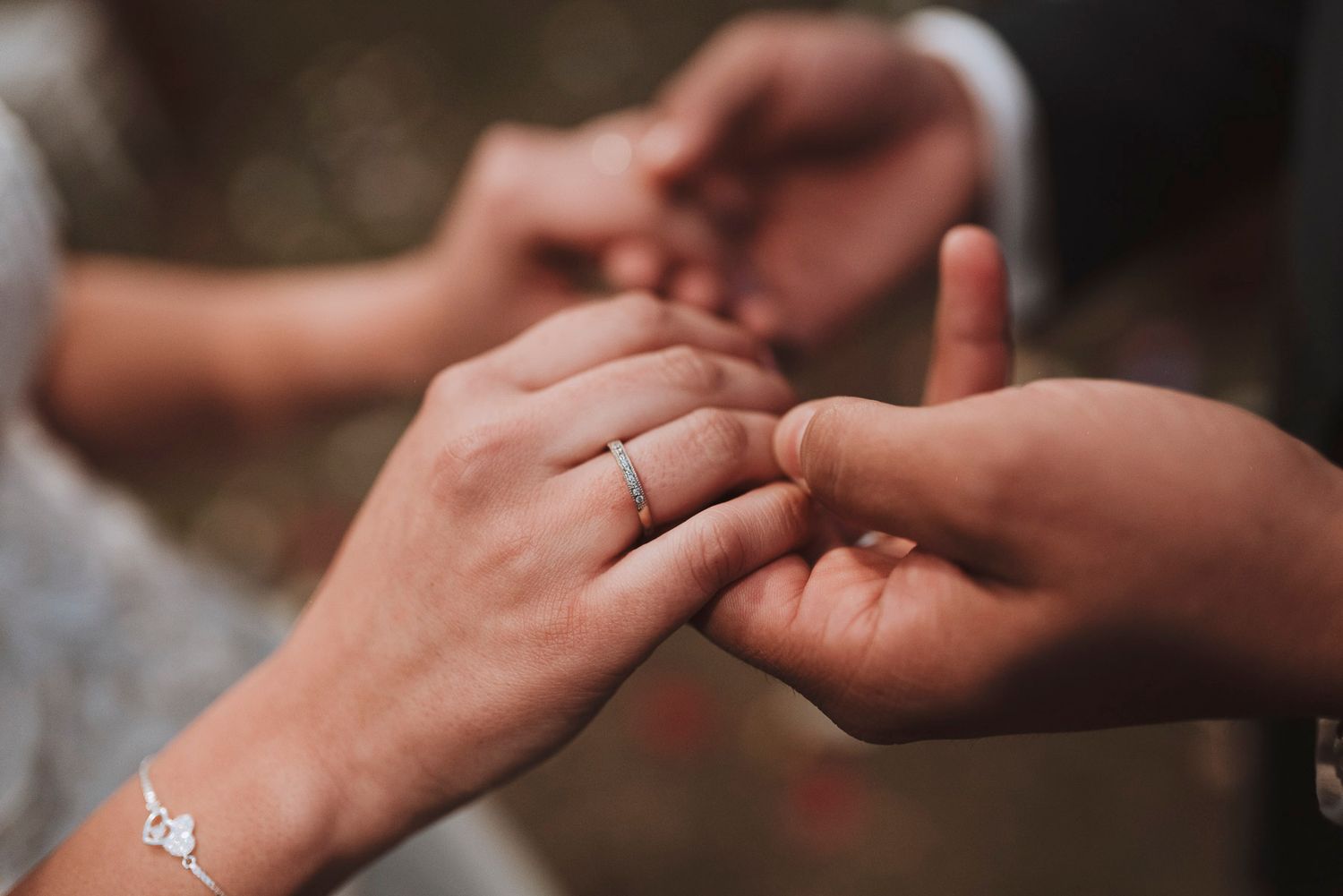 Close up view of hands holding a delicate engagement ring in various romantic poses outdoors.