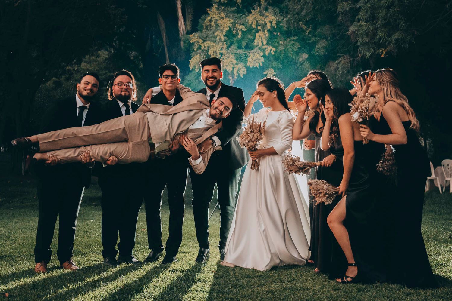 Wedding party poses outdoors under trees creating a fun dramatic scene.
