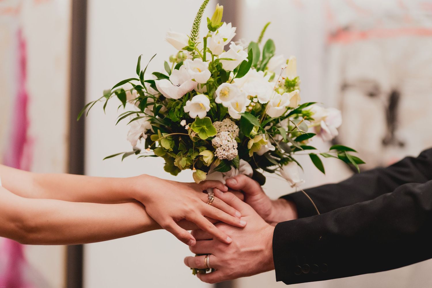 Hands exchanging a beautiful bouquet of white and pink flowers with delicate greenery during a special occasion.