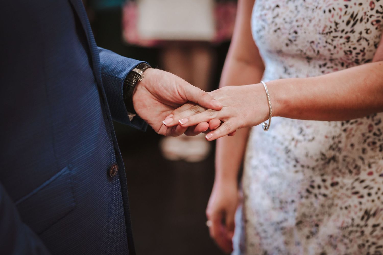 A couple holds hands intimately during an outdoor wedding ceremony with a soft sunlit glow.