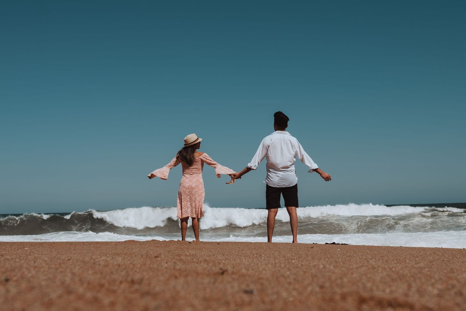 Couple standing on beach enjoying ocean waves and shoreline views at sunset.