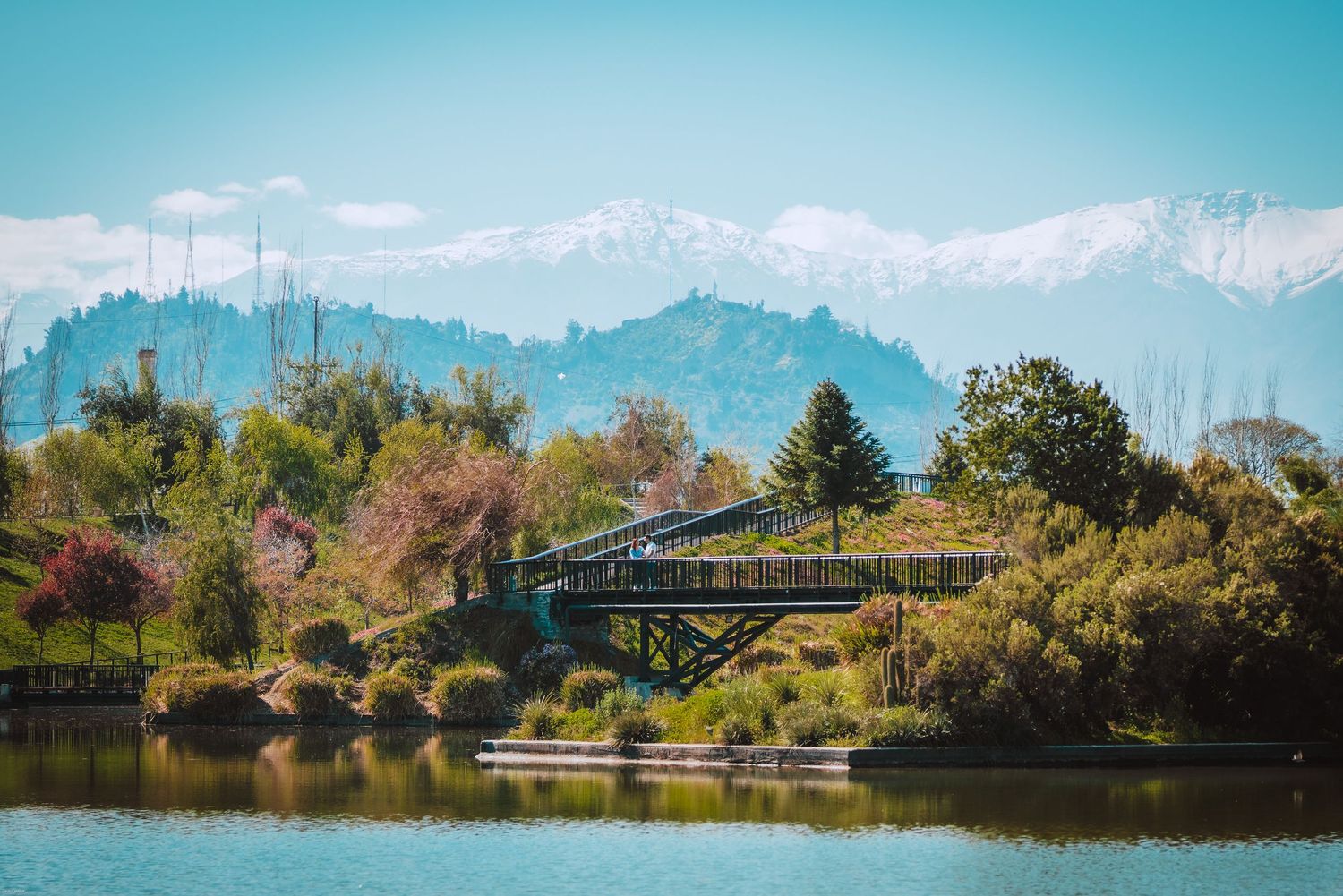 Scenic mountain landscape with a bridge over calm waters and autumn foliage.