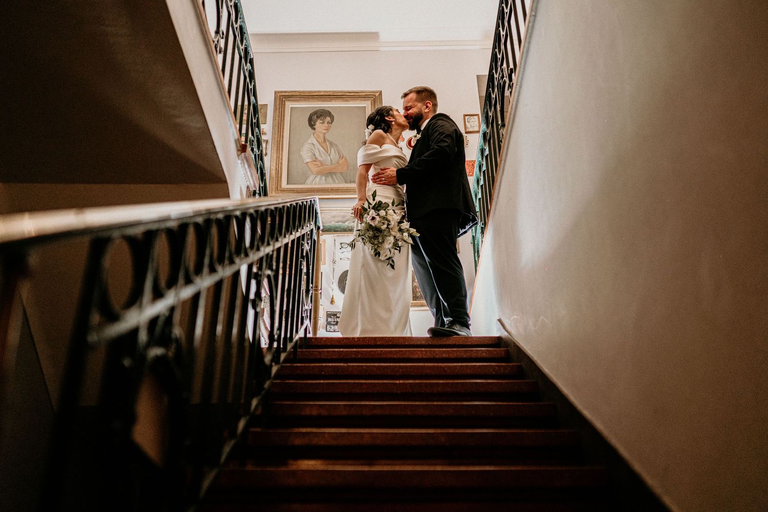 A bride and groom walk up an elegant spiral staircase decorated with wooden banisters.