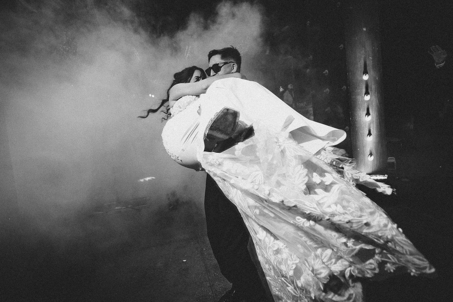 Dramatic black and white photo of dancing couple with flowing wedding dress in smoke.