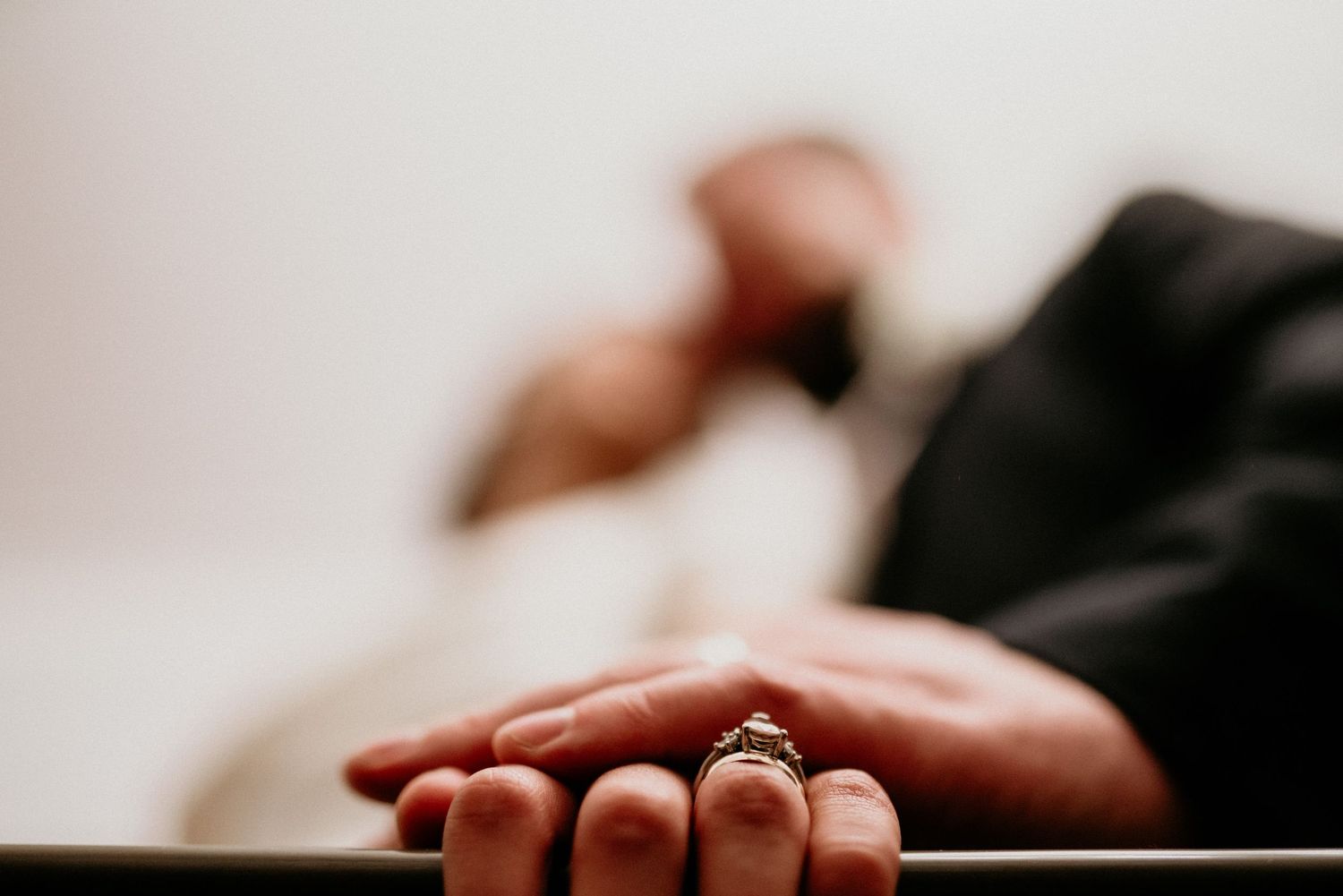 Close up photo of an engagement ring on a hand against a light neutral background.