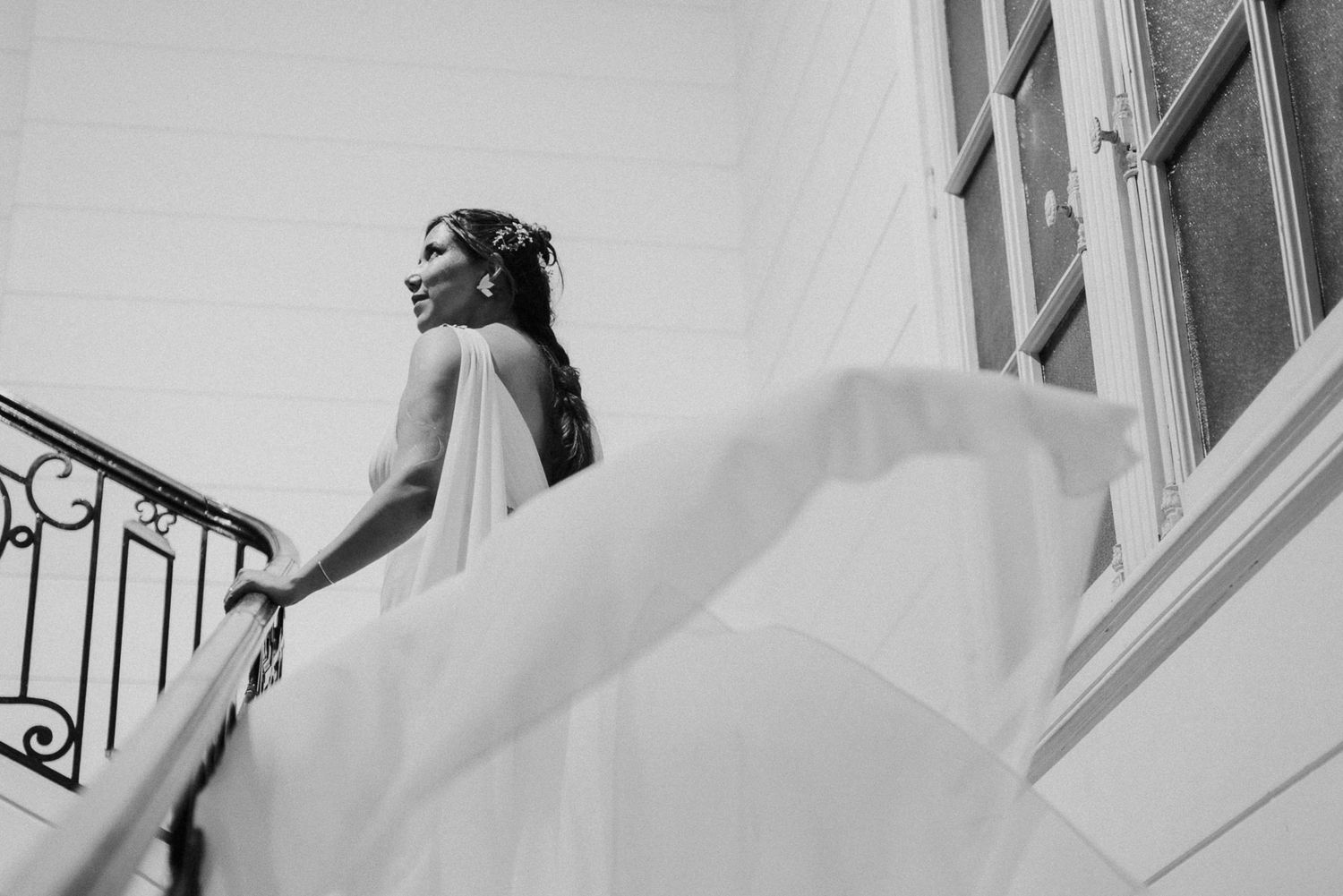 A flowing white wedding dress billows dramatically as the wearer descends an elegant staircase with ornate railings.