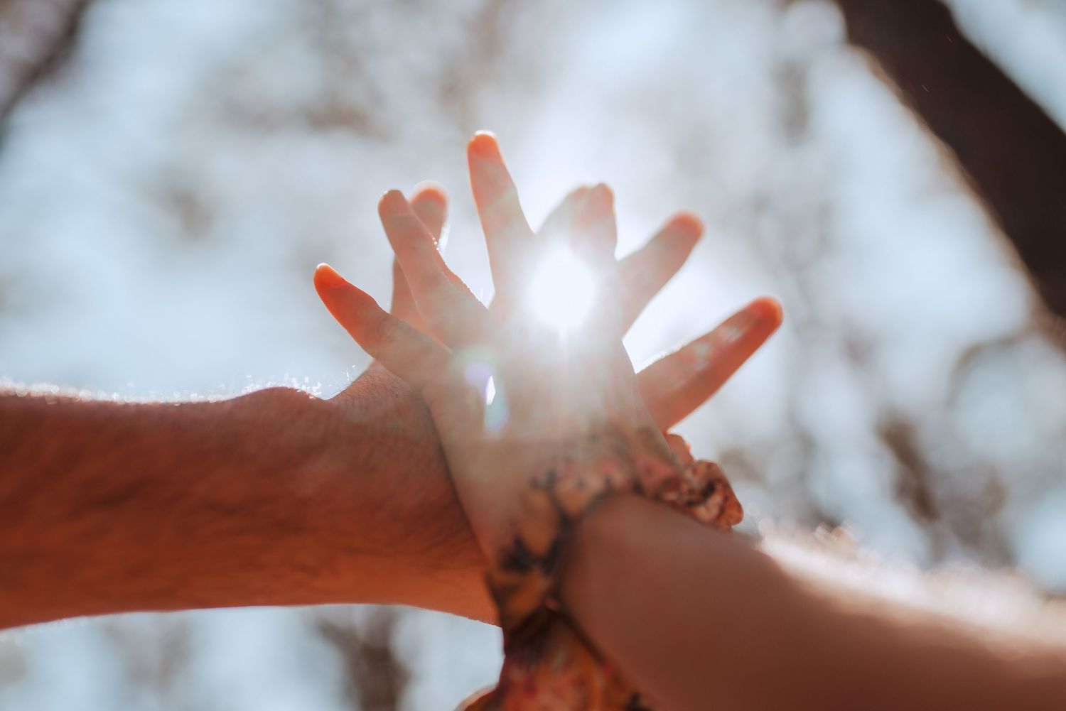 Hands reaching up towards bright sunlight creating artistic silhouette effect.